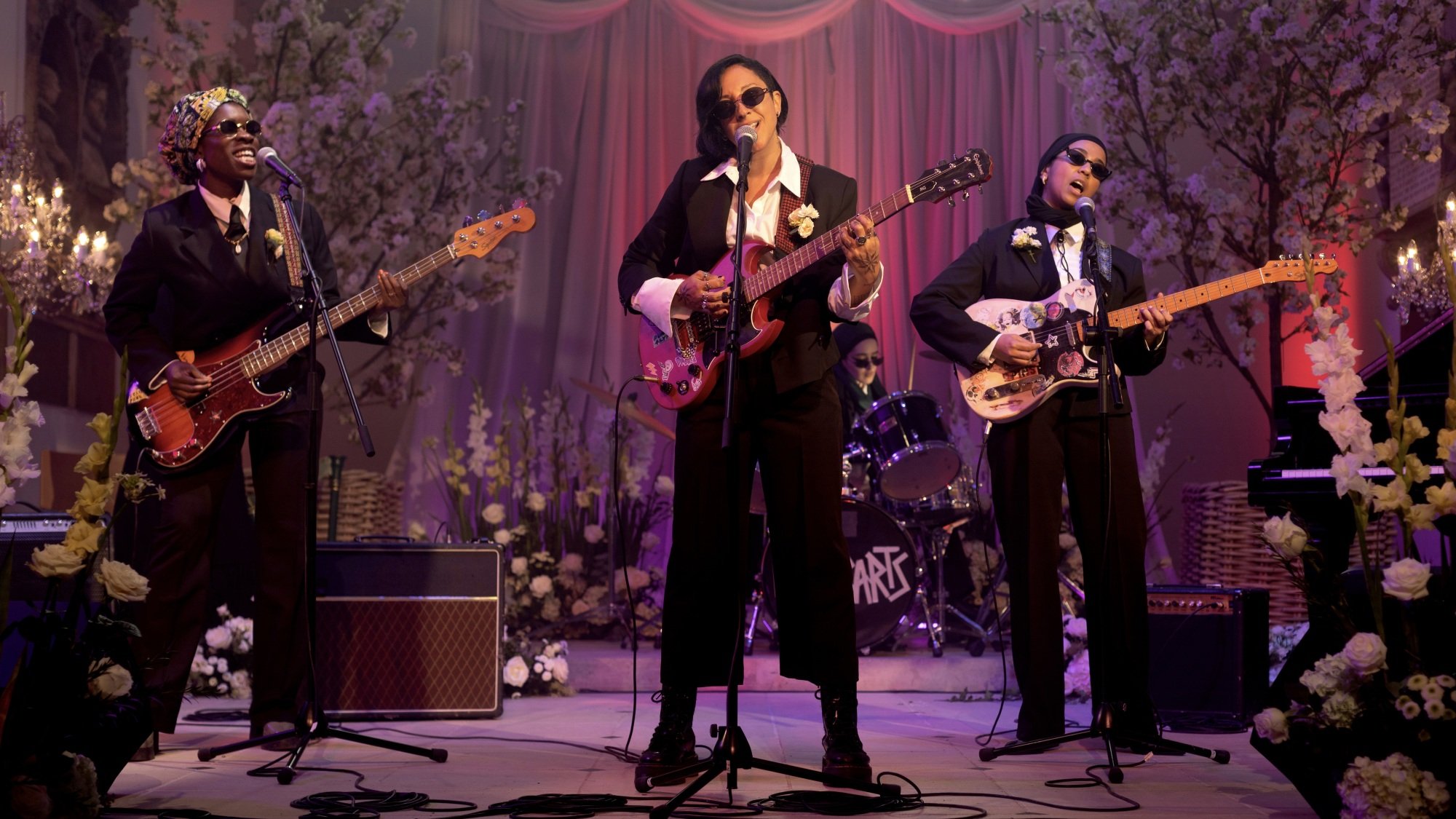 Four women in suits, some wearing head coverings, play in a rock band in a church.