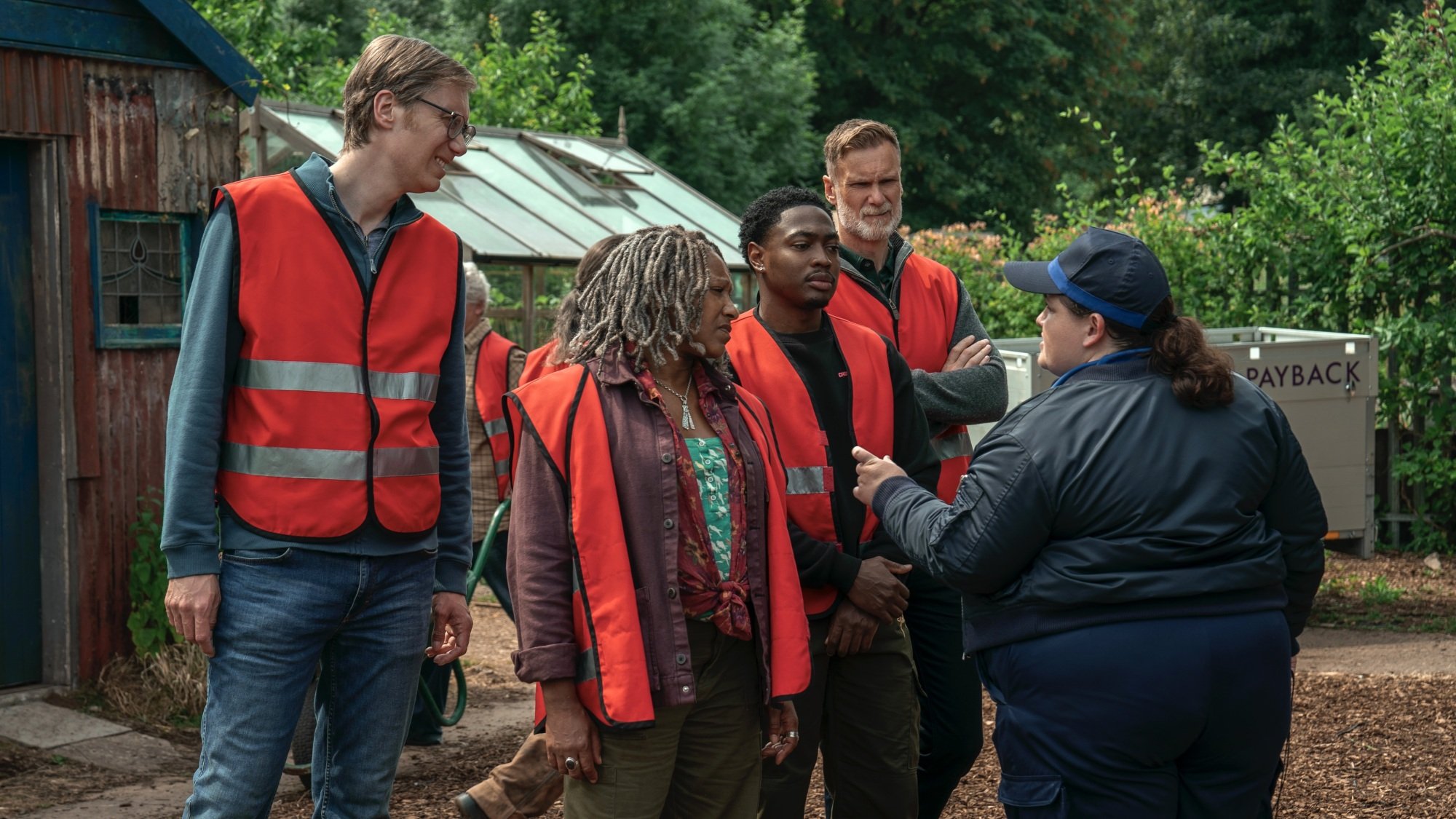A group of men and women in red vests outside a community garden.