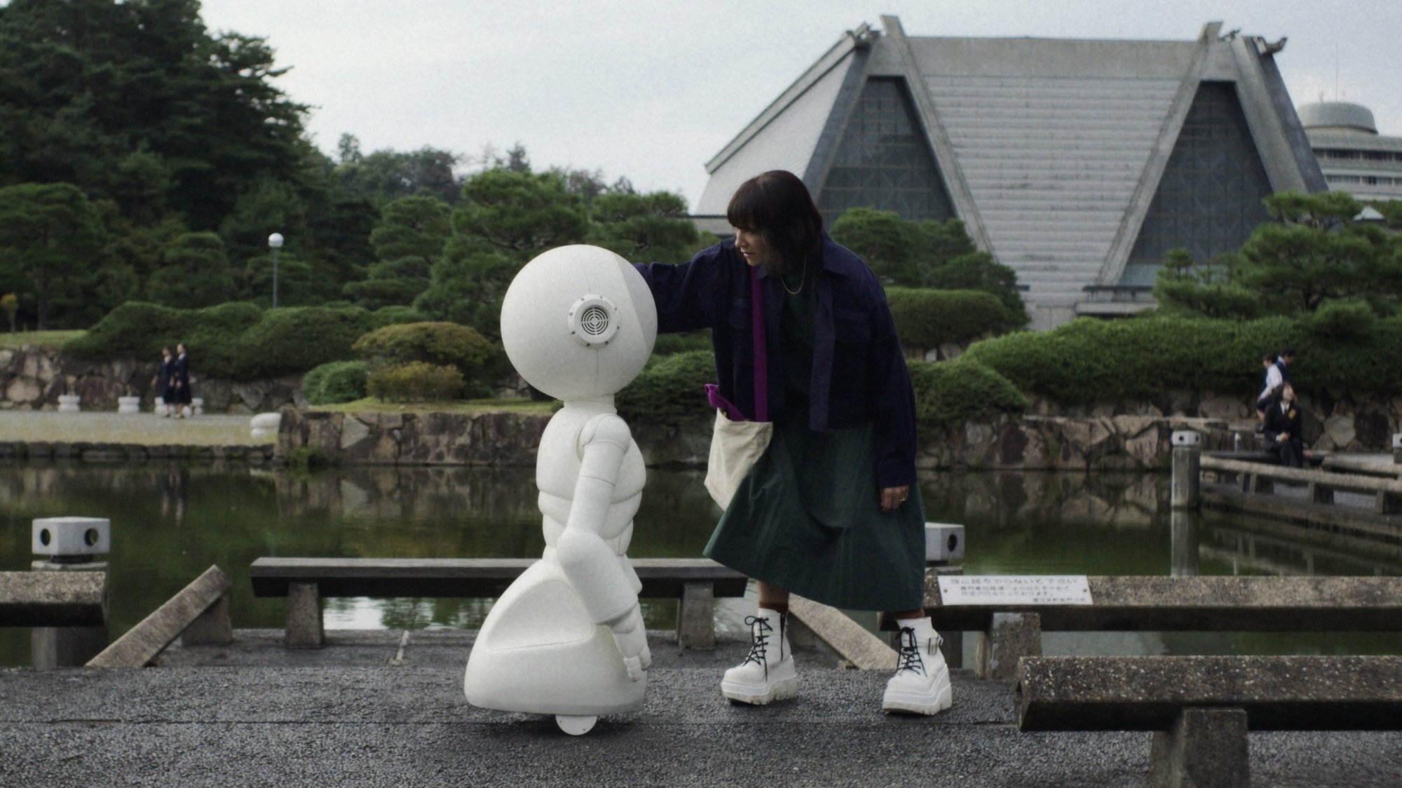 A woman pets a large white robot on the head.