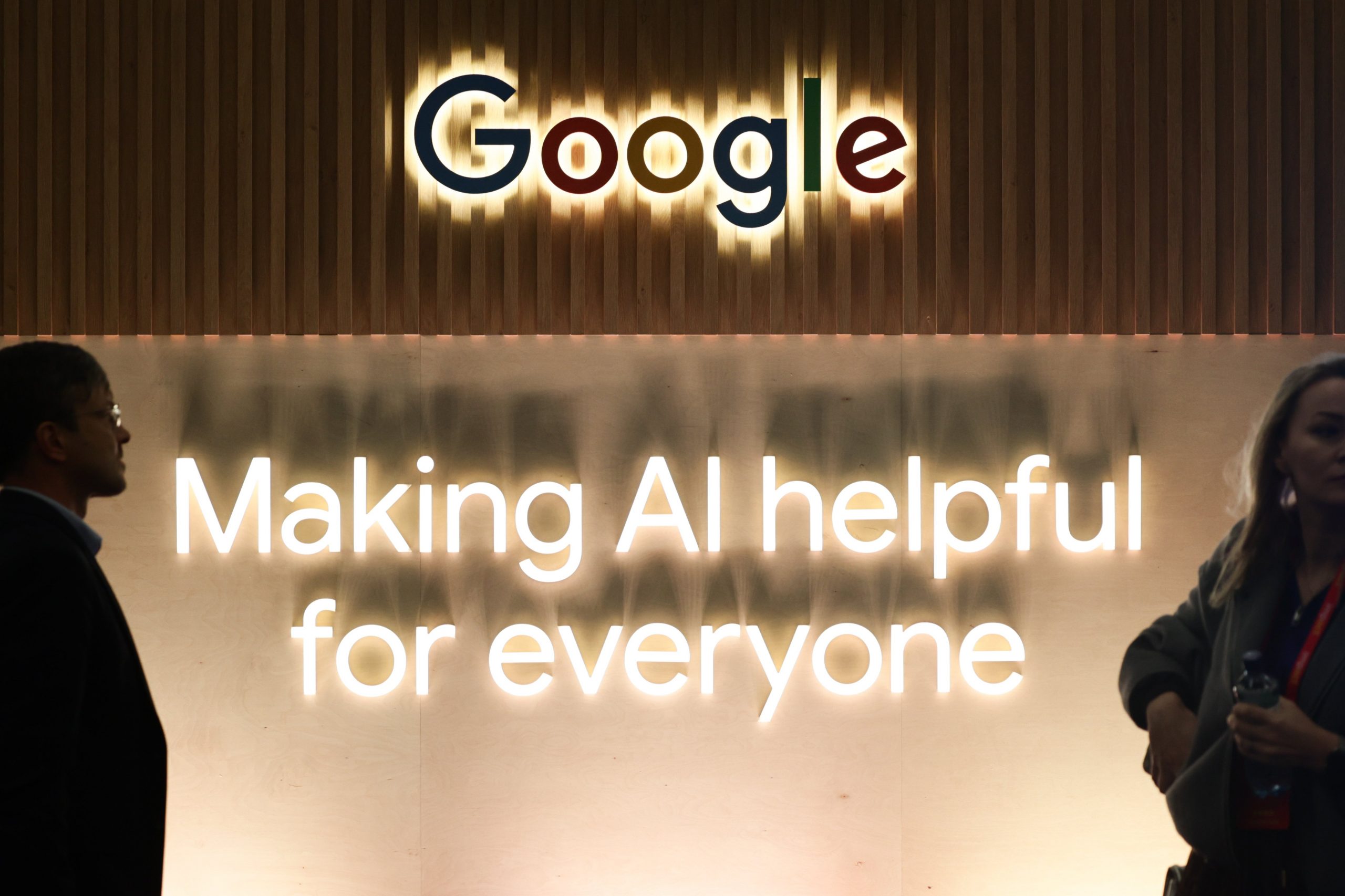 People in front of the Google logo on a wall above a slogan about making AI helpful for everyone