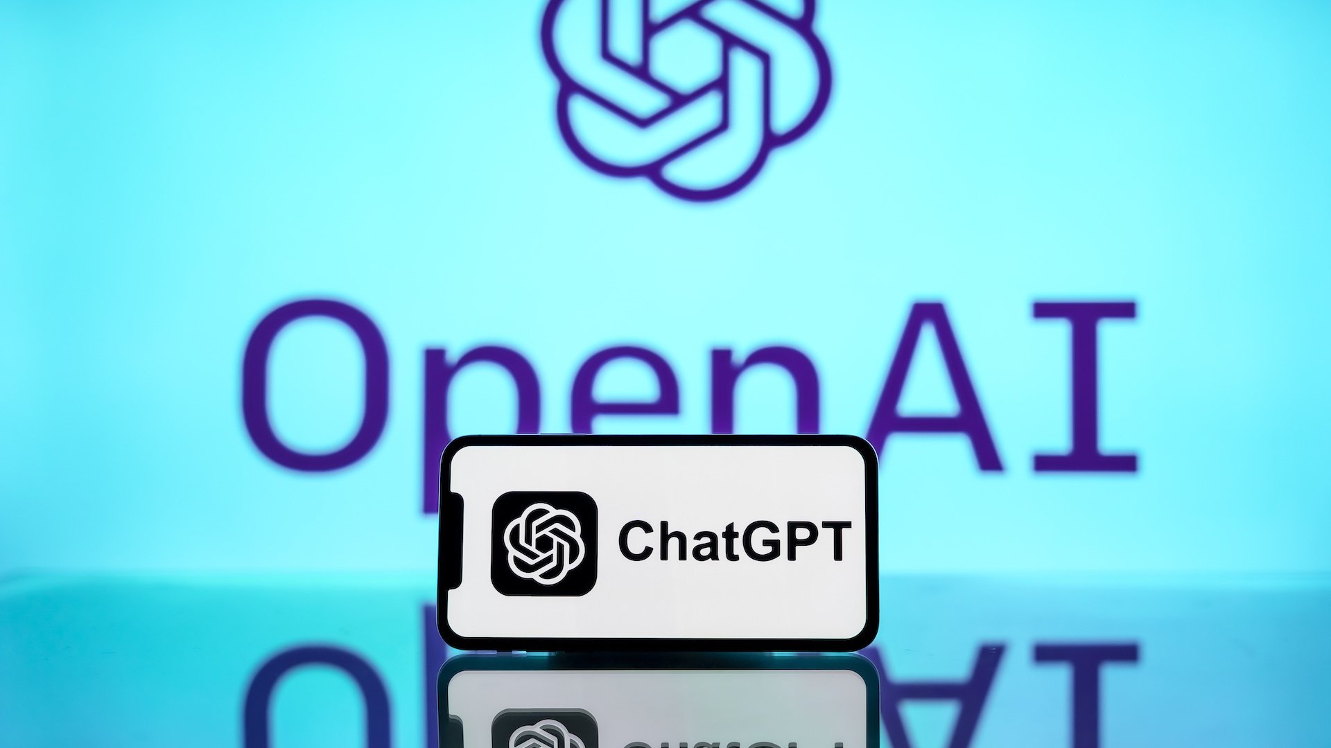 The ChatGPT logo is seen displayed on a mobile phone screen with OpenAI logo in the background.