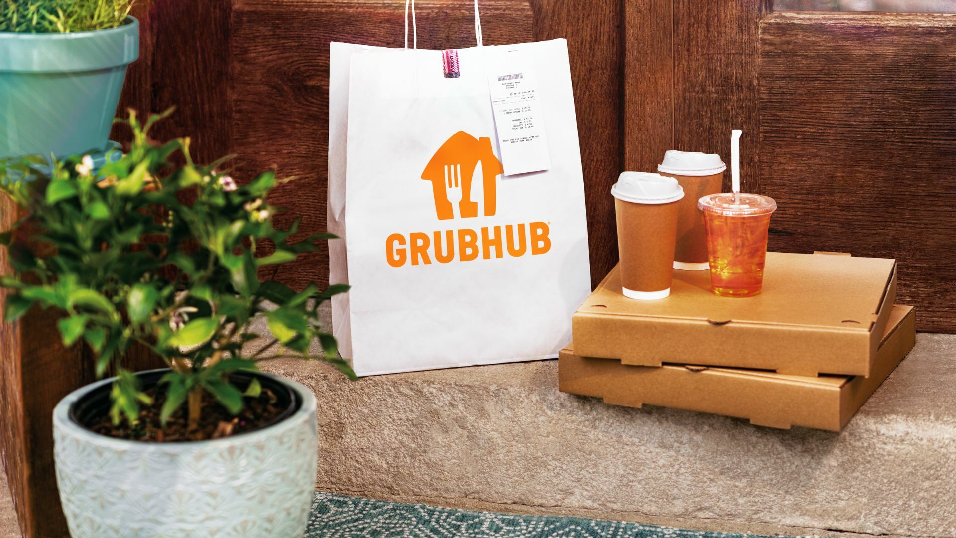 A Grubhub delivery bag on a doorstep, next to pizza boxes and drinks.