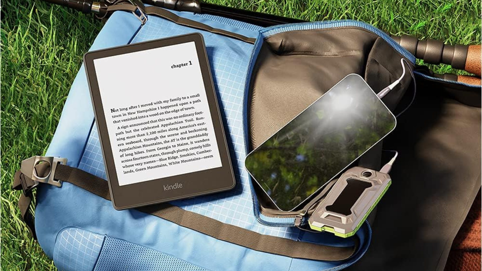 A Kindle Paperwhite sitting on a backback next to a smartphone