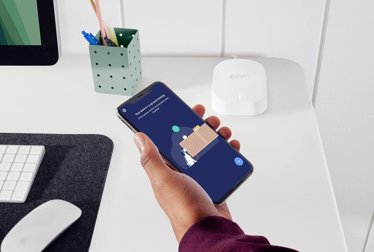 person holding smartphone next to eero router 