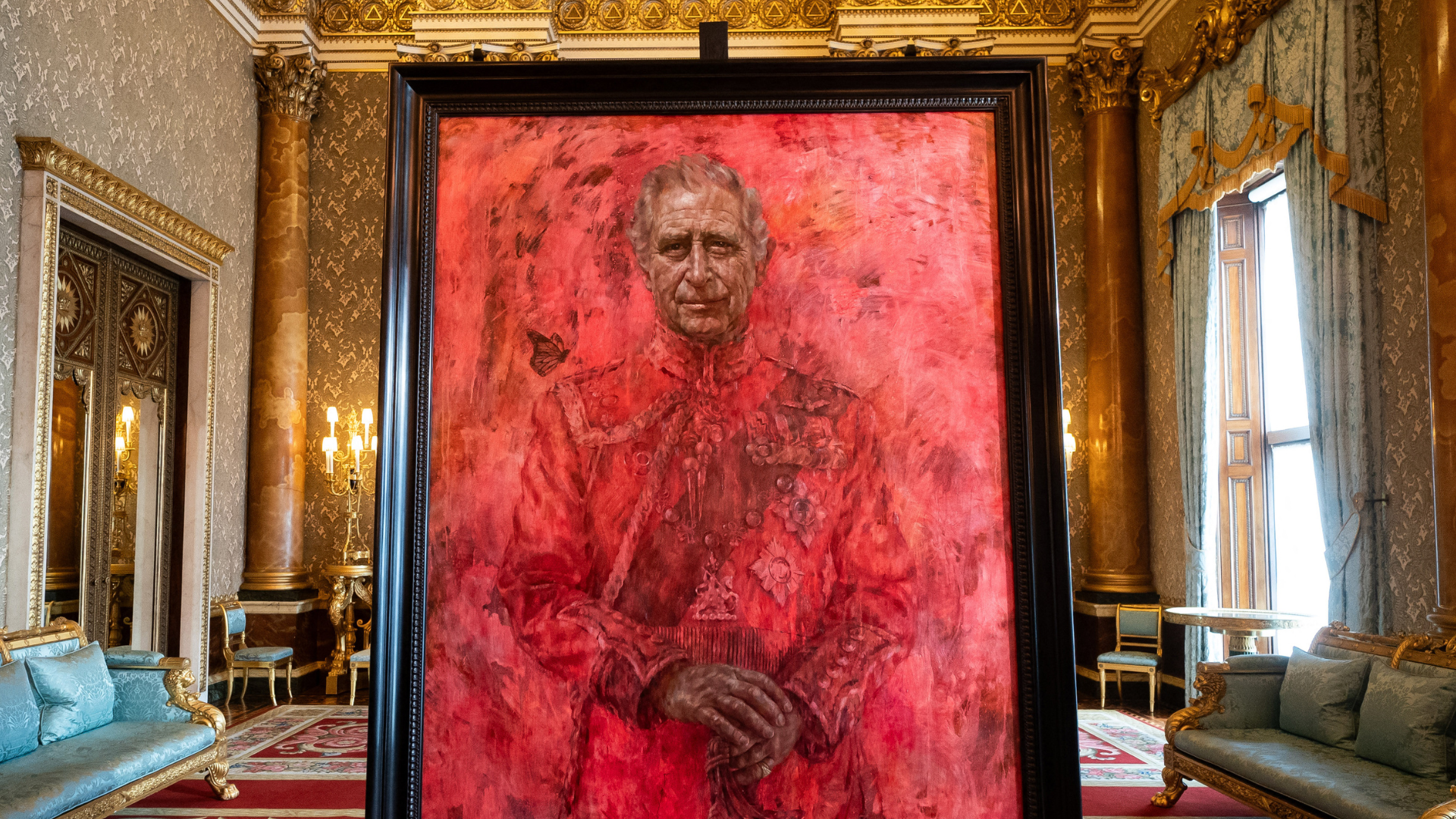A portrait of King Charles in a black frame. The portrait is mostly red, and a butterfly is about to rest on the King's shoulder.