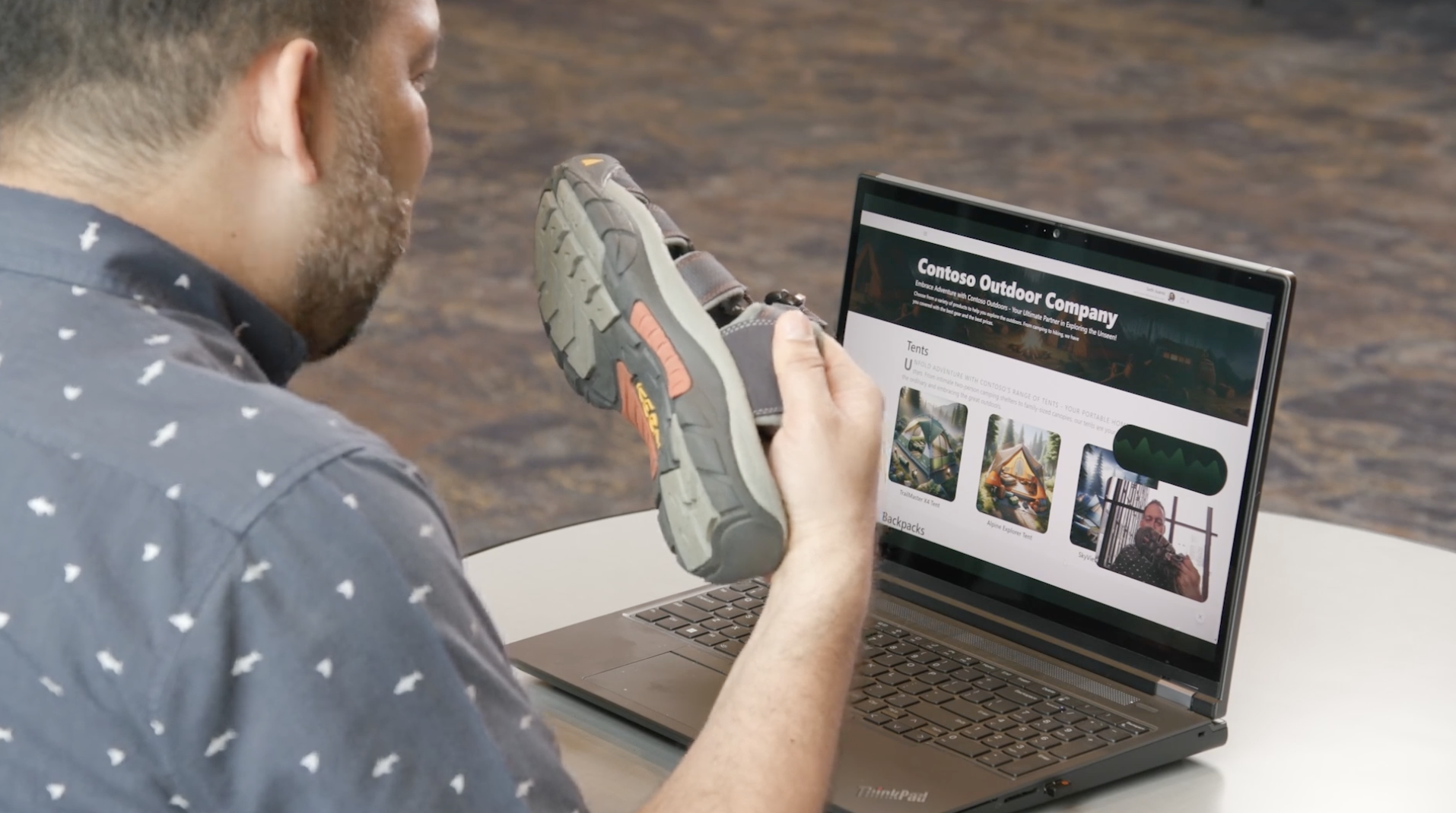 Man in blue shirt holding a hiking sandal in front of a computer