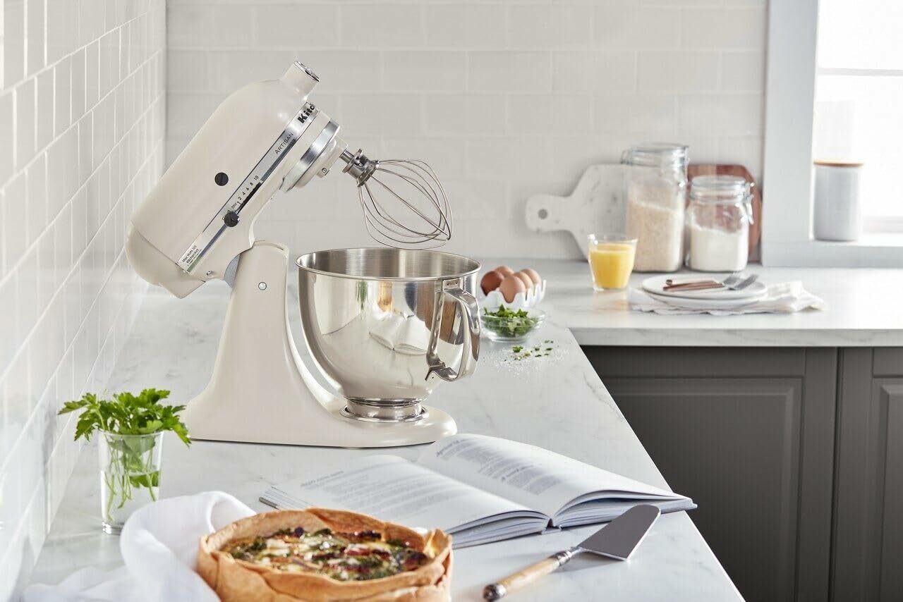 A KitchenAid mixer sits on a kitchen countertop with a recipe book and a quiche