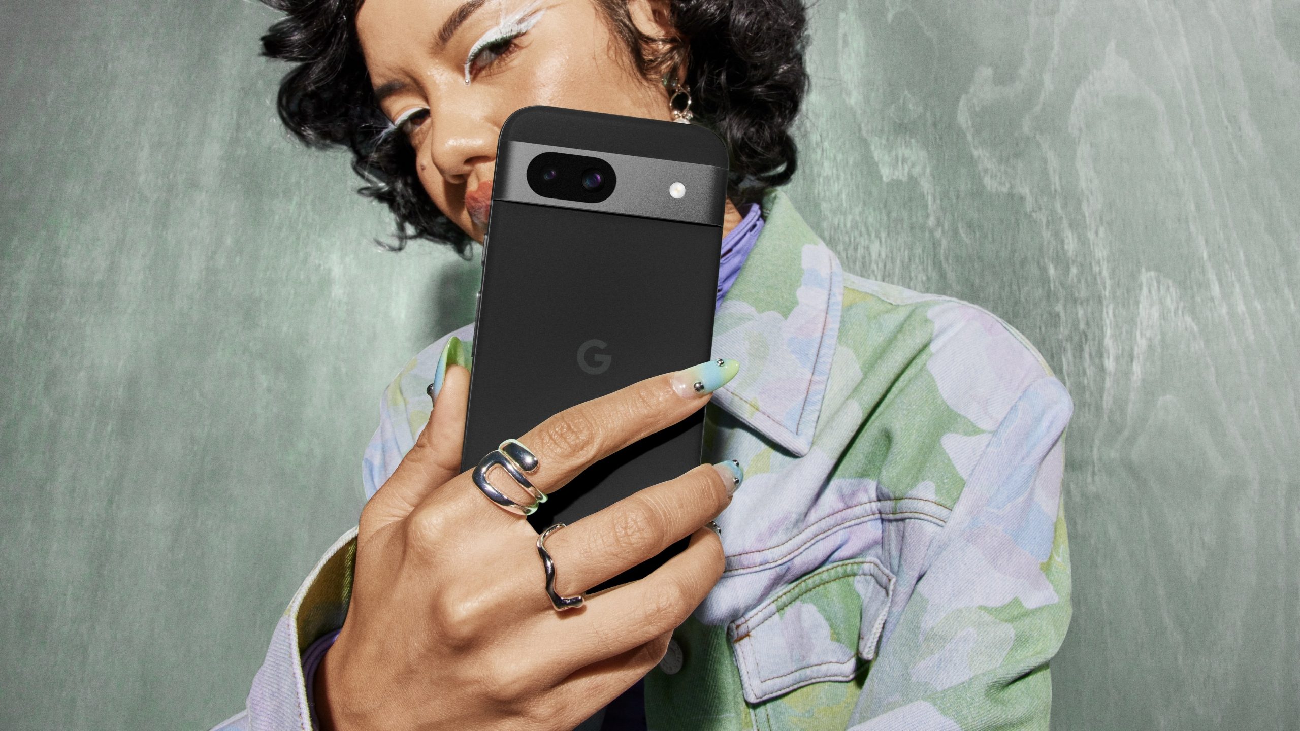 person on a blue background holding google pixel 8a in obsidian