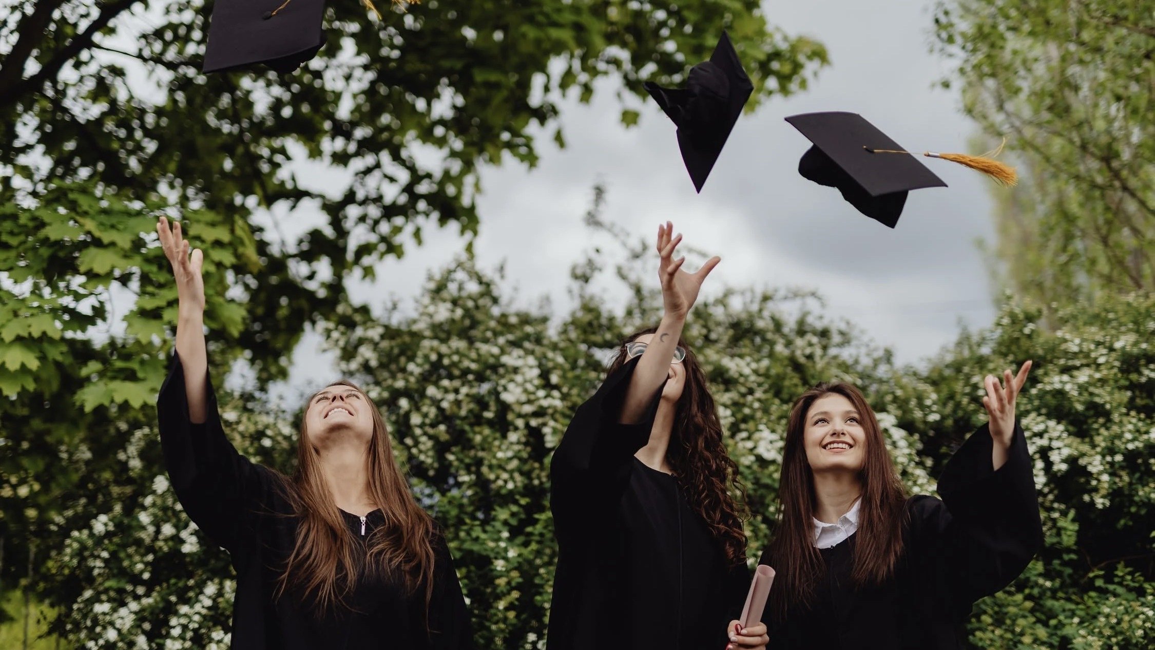 Three people throwing their graduation cap to the sky.