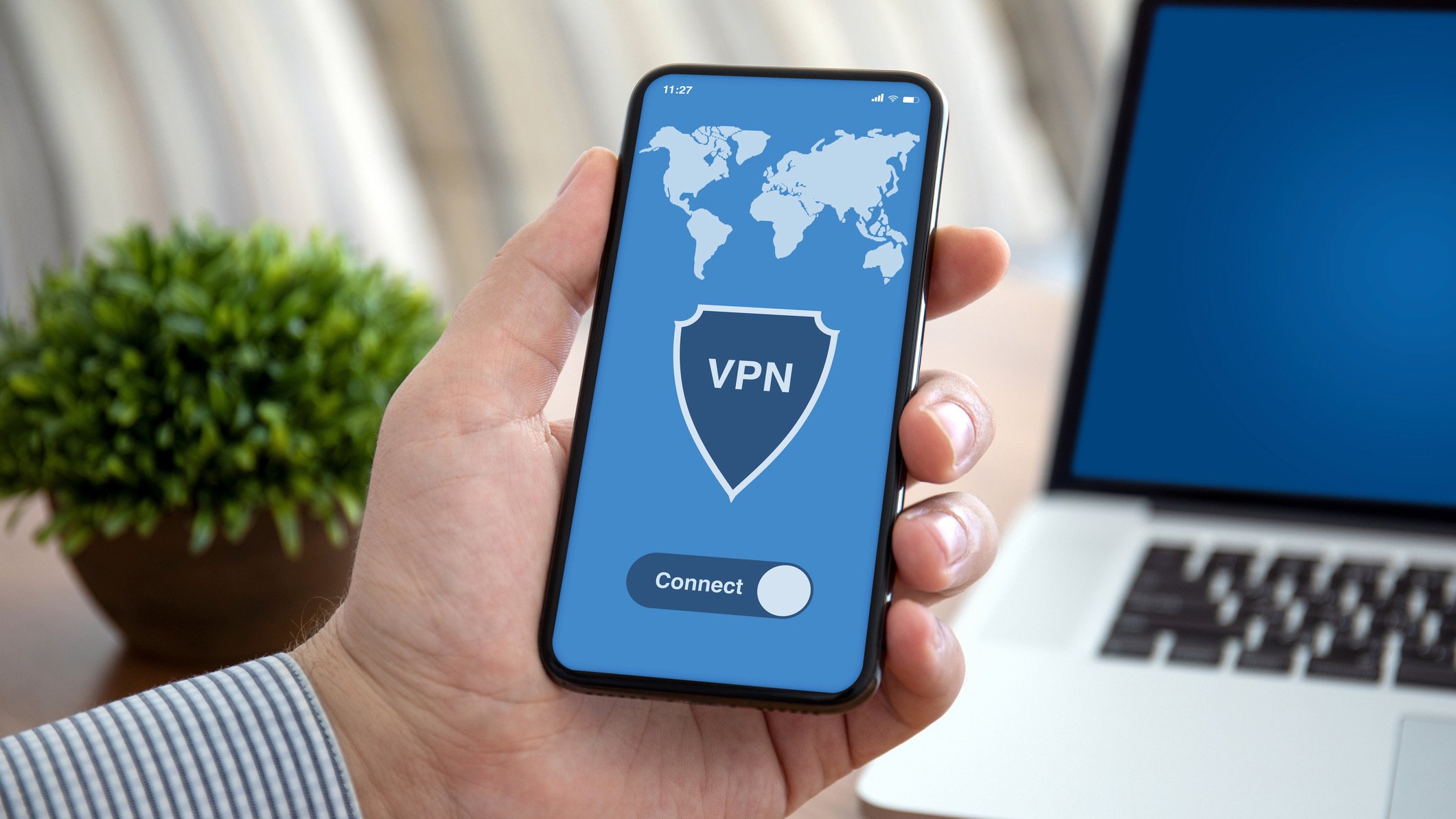 man holding smartphone in front of laptop, phone screen reads 'VPN'