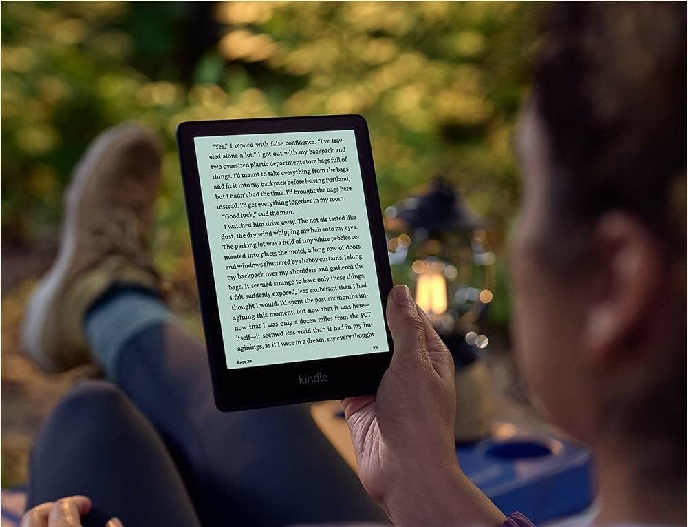 a person reads a book on an amazon kindle ereader while sitting in the woods