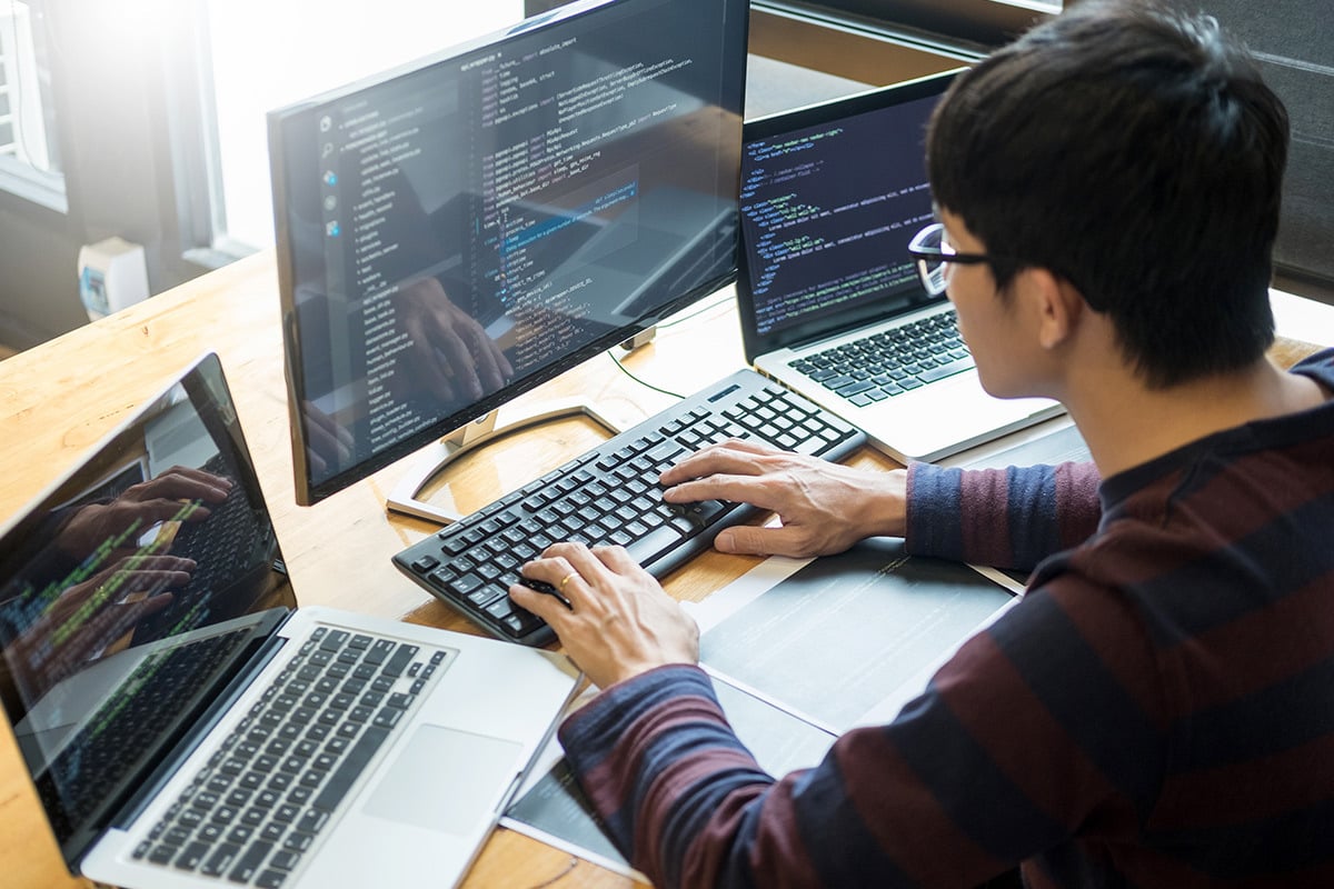 Man coding on three screens. 