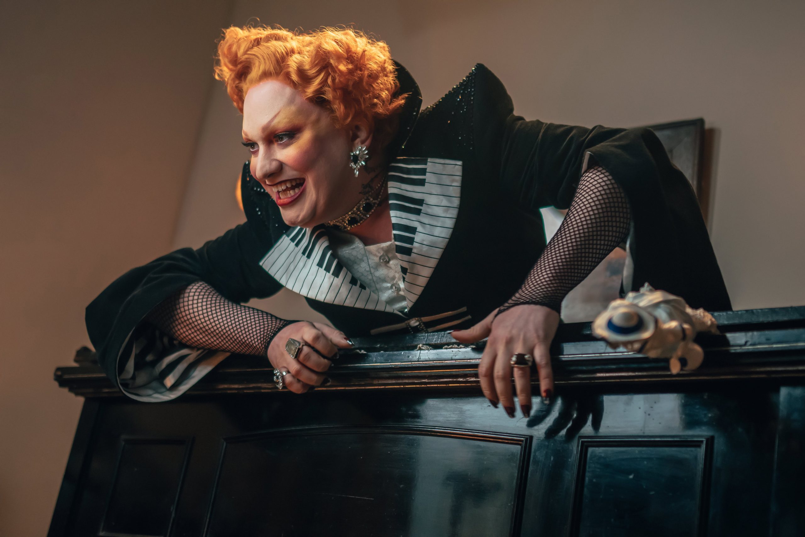 Jinkx Monsoon dressed as the Maestro atop a piano