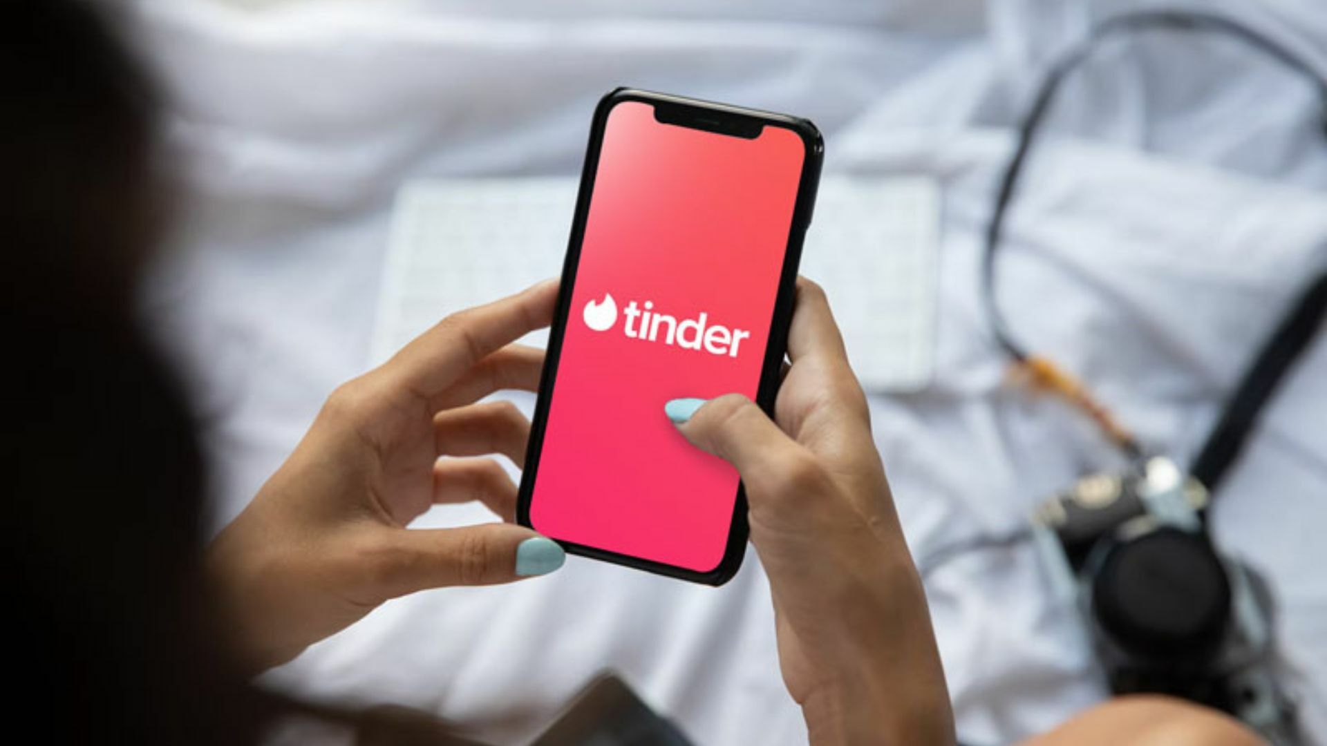 A person holding a phone showing the Tinder logo.