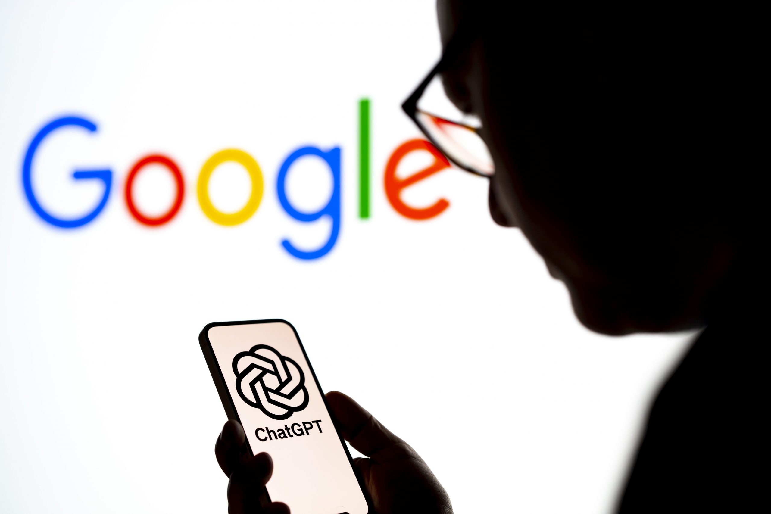 User looking at OpenAI ChatGPT logo on smartphone with Google logo in the background
