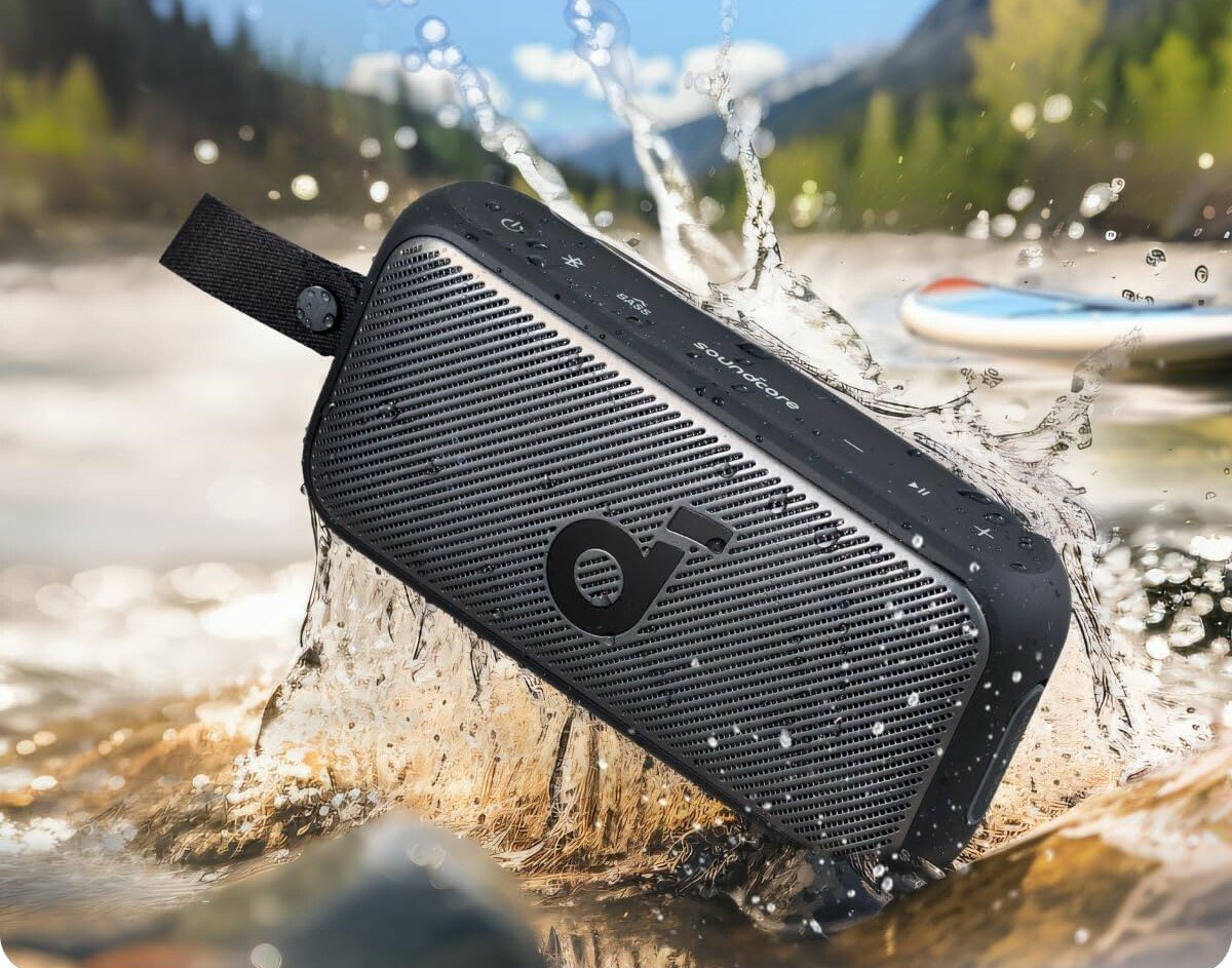 a black soundcore speaker dips into the water of a river with slashing surrounding the speaker on a sunny day