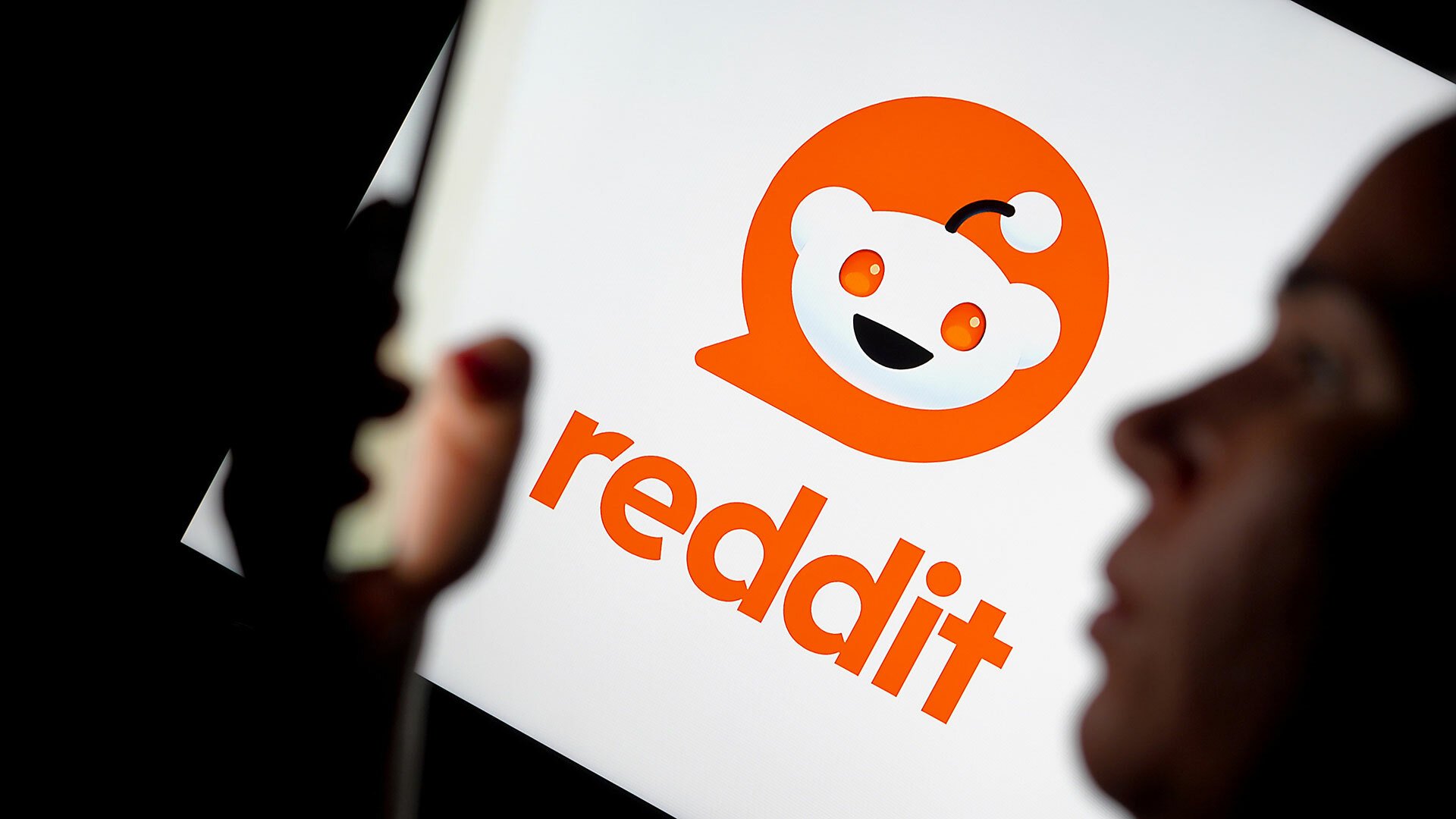 The Reddit logo is visible in the background, while the silhouette of a woman using a smartphone can be seen in the foreground.