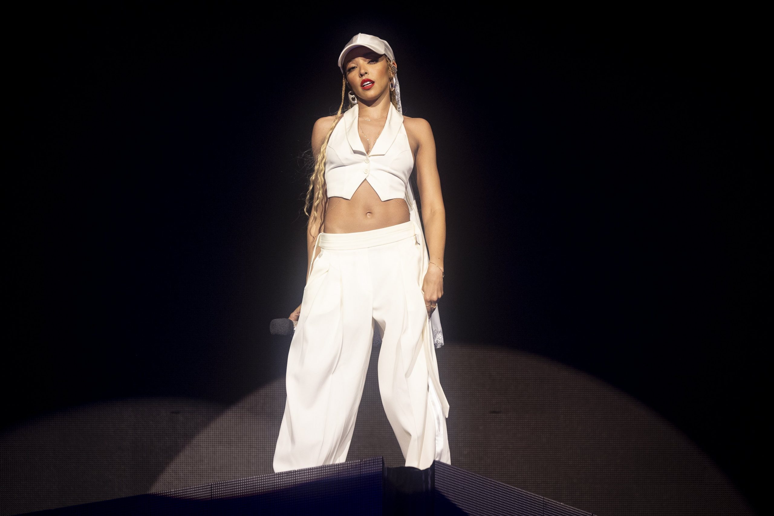 Tinashe performing at Coachella in a white vest, pants, and baseball cap. 