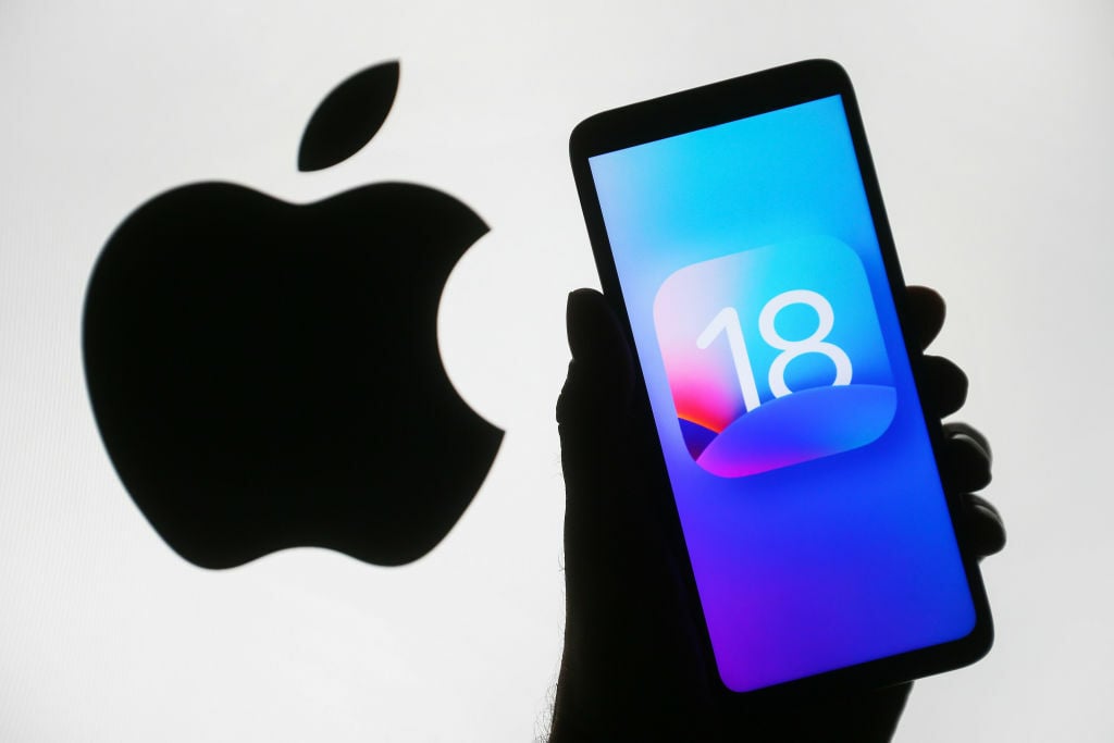 ios 18 logo on a smartphone in front of a background that shows the apple logo