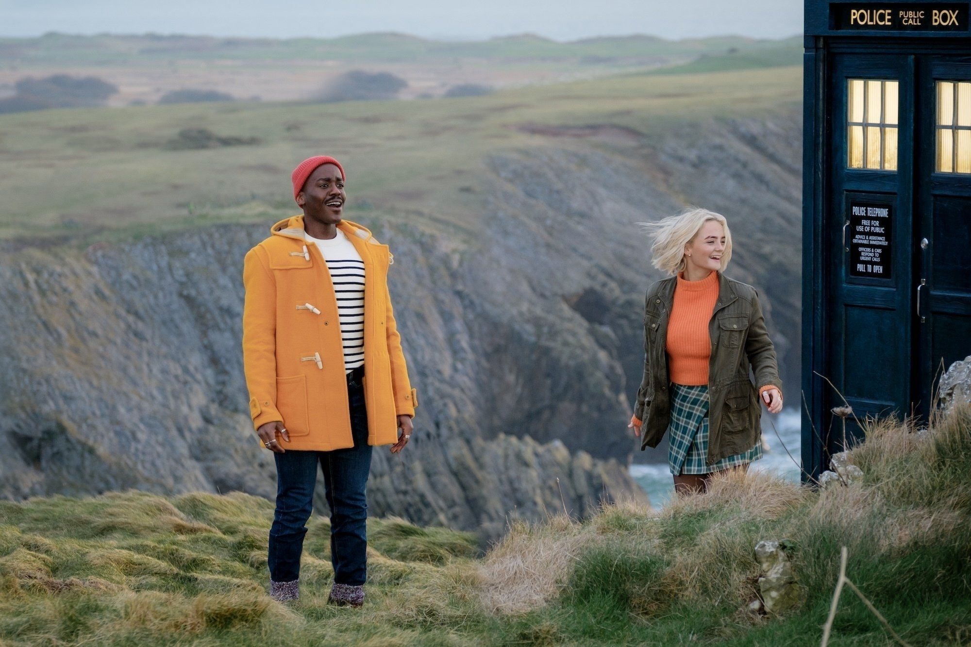 The Doctor in a yellow jacket and Ruby, on a cliff next to theTARDIS