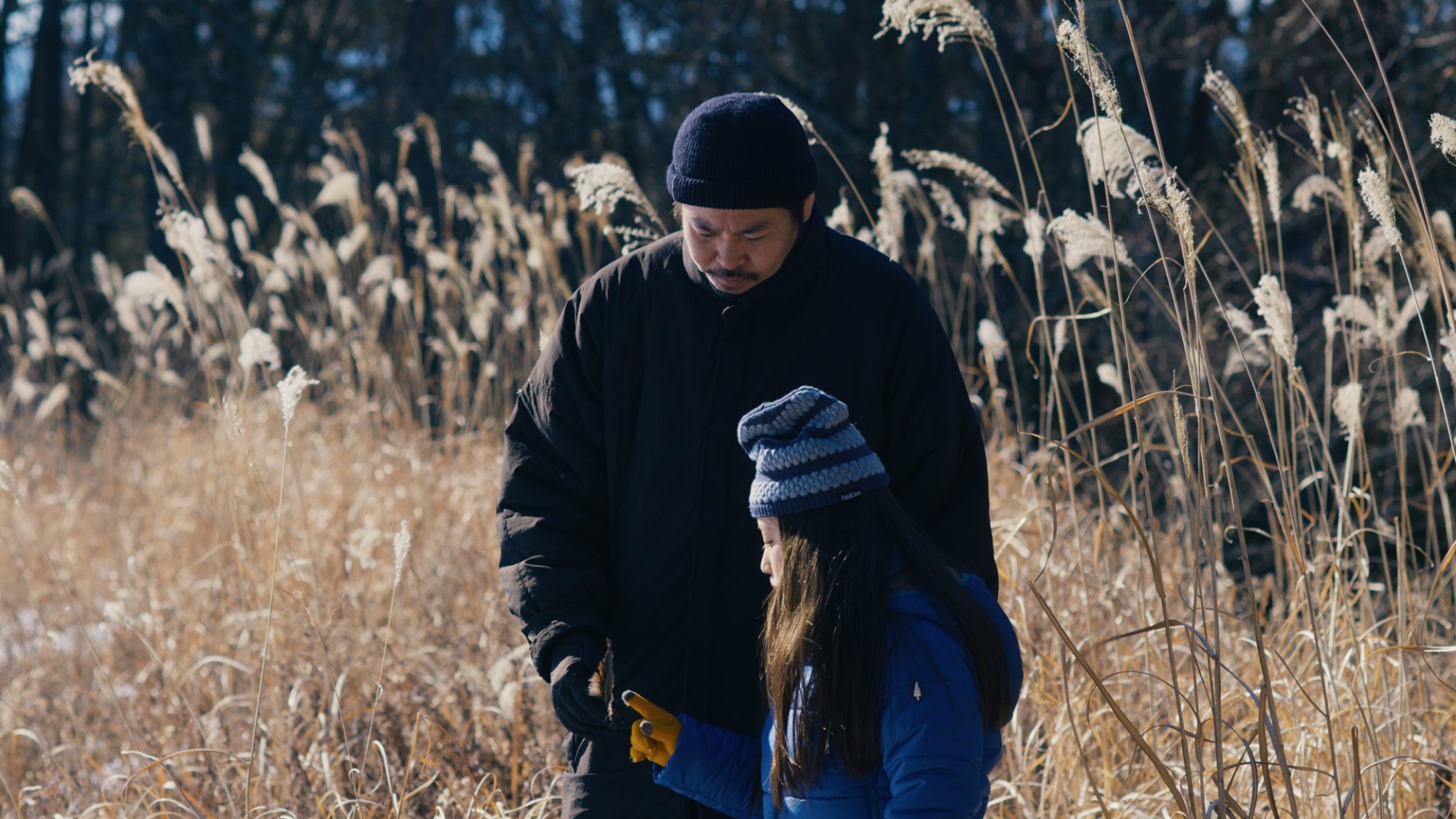 A man and a girl stand in a field in winter clothing, having a conversation.