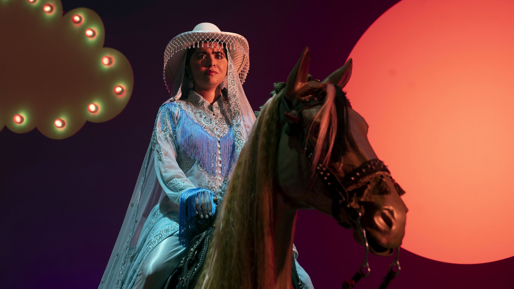 Malala Yousafzai sits on a fake horse in the show "We Are Lady Parts"