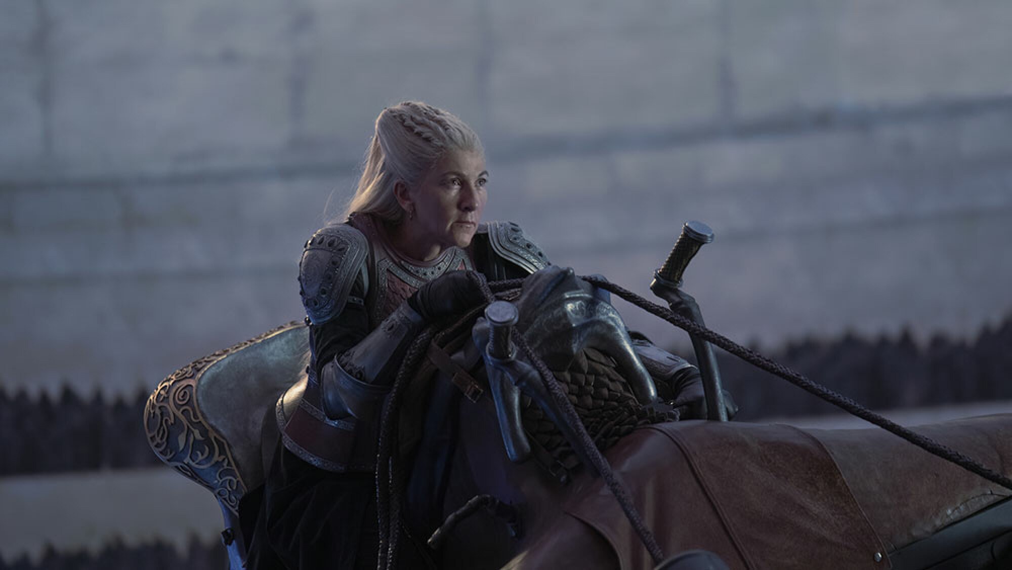 A woman with white hair rides on the back of a dragon indoors.