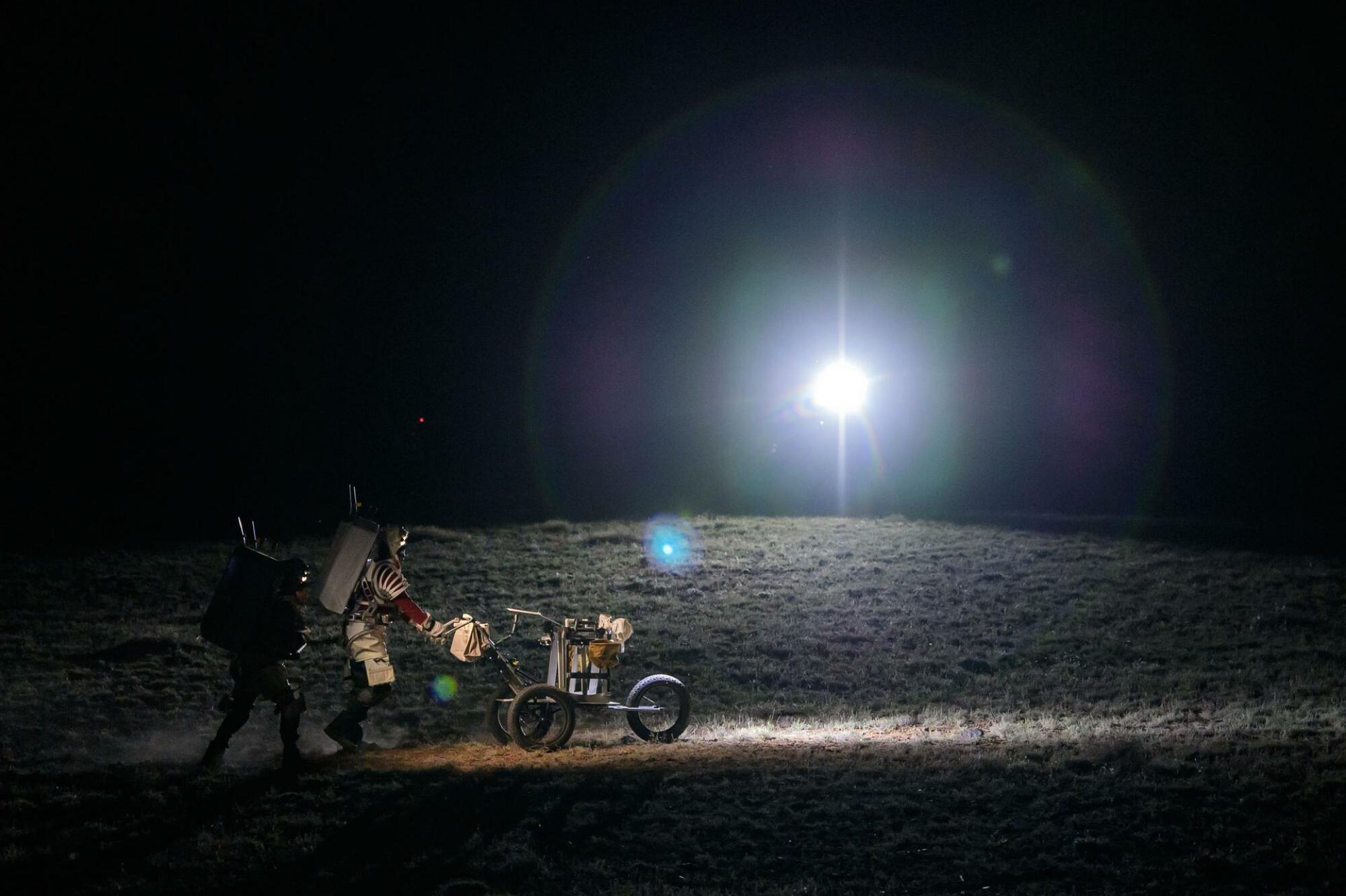 The two astronauts pushing a tool cart across the desert surface.