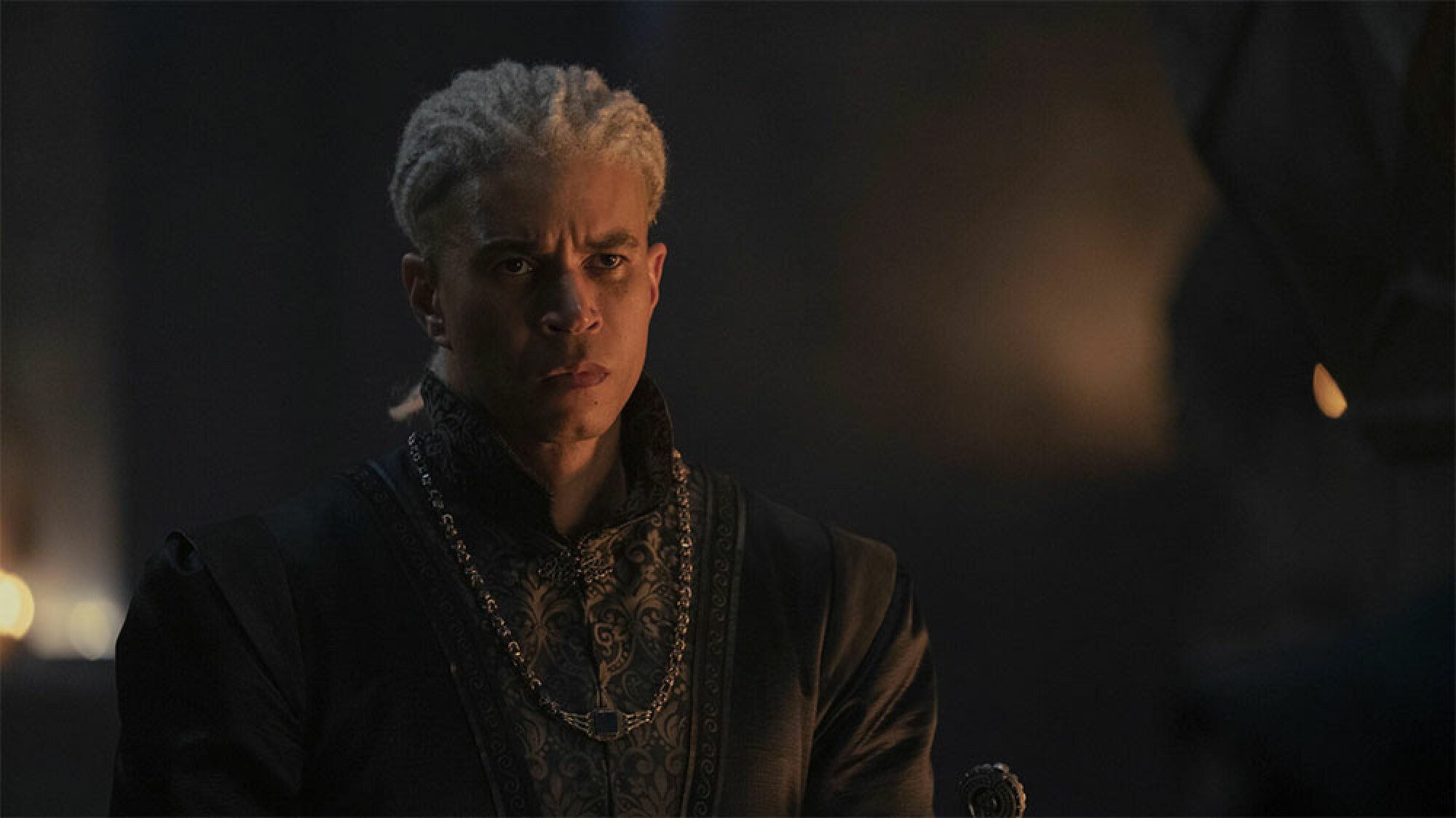 A man with white hair stands in a dark room.