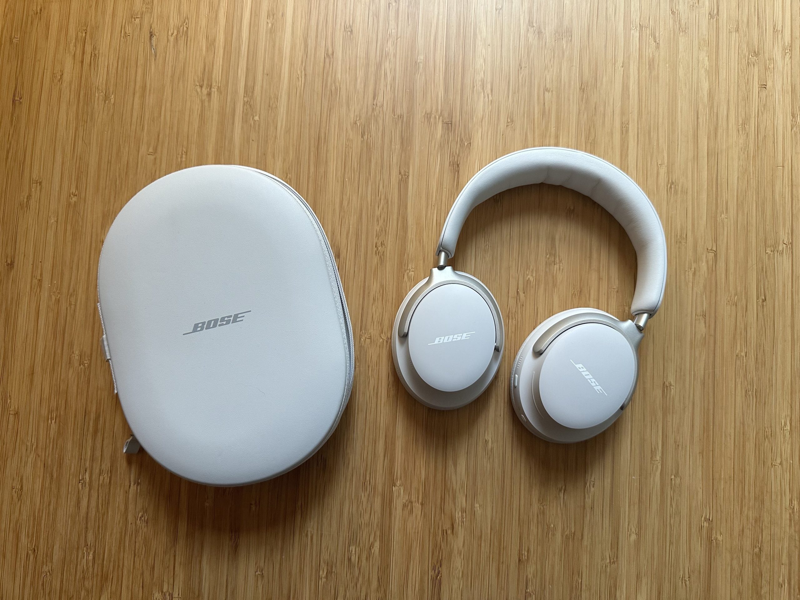 A pair of Bose QuietComfort Ultra headphones with case on wood surface