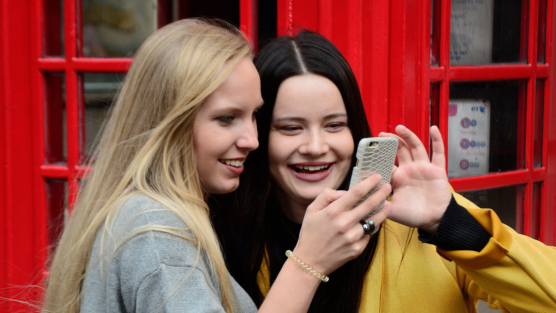 Two young women crowd together to look at a phone screen.