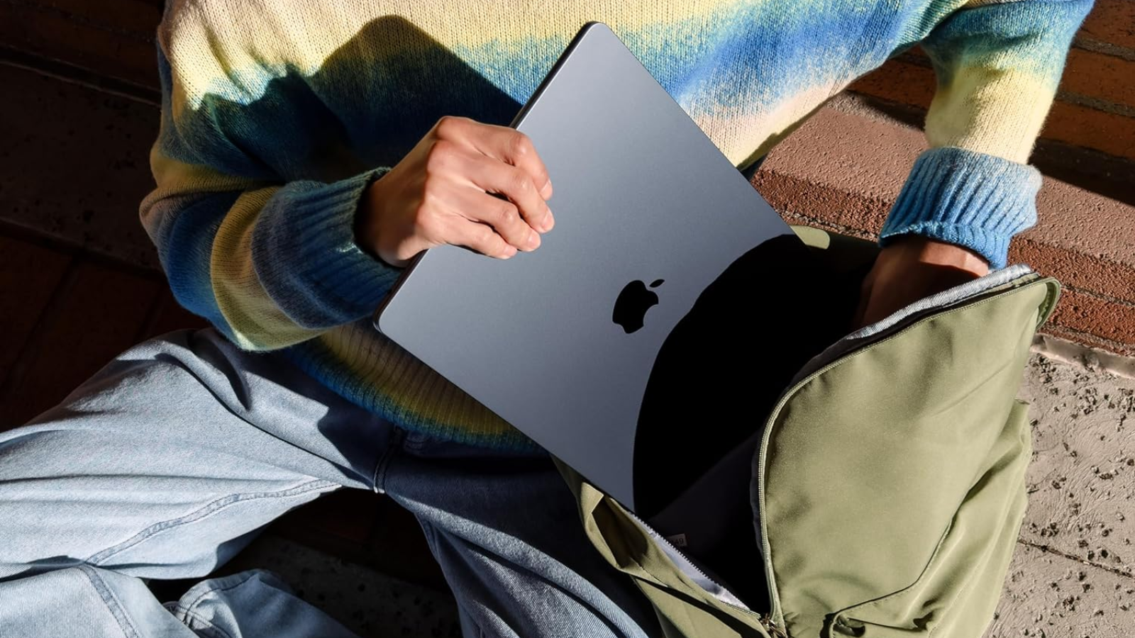 a close-up of a person putting a 15-inch apple macbook air into a backpack