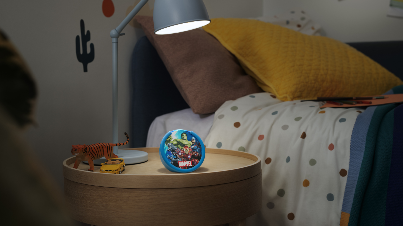 an echo pop kids sitting on a child's bedside table with a desk lamp shining on it