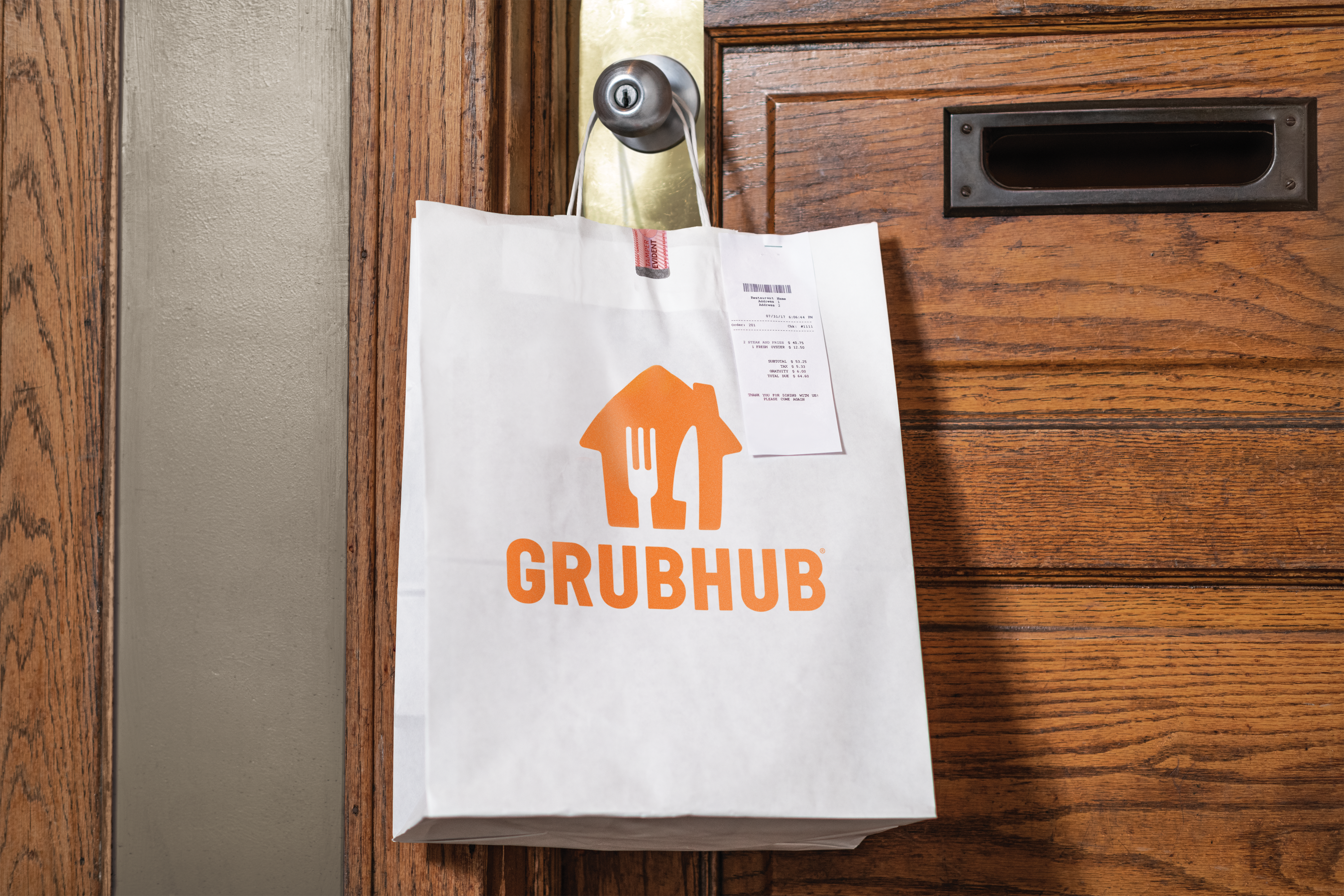 a white paper bag with a grubhub logo hangs on the doorknob of a front door