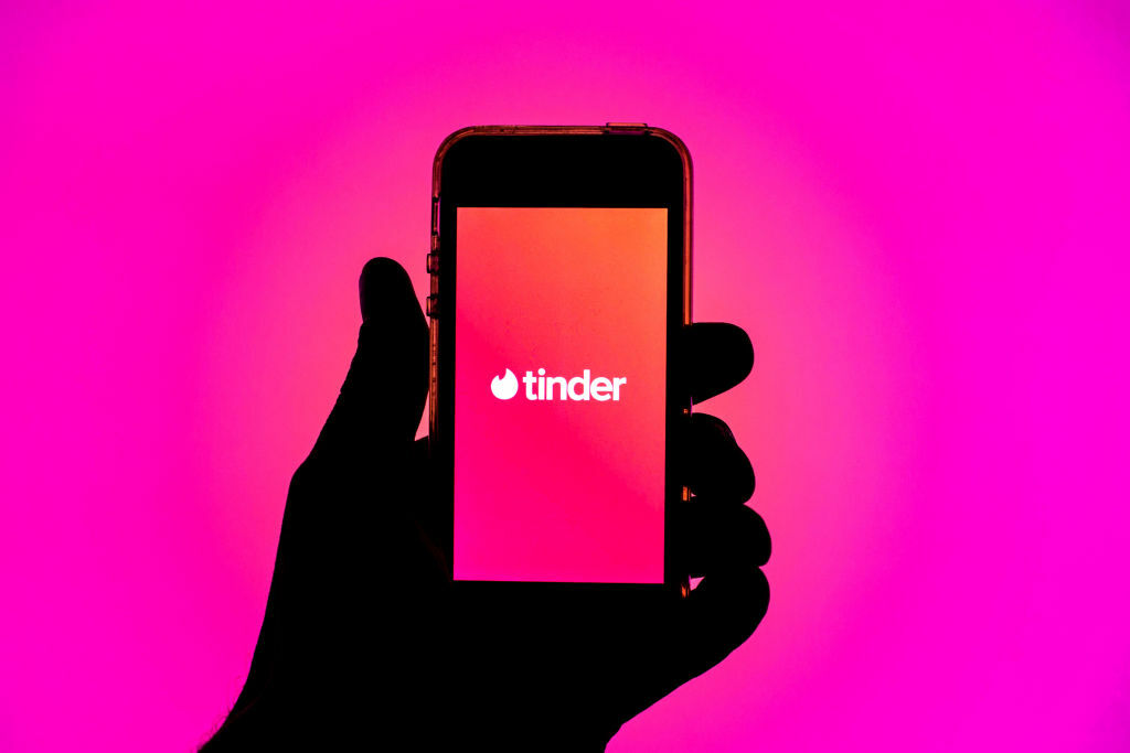 Silhouette of a hand holding a smartphone displaying the Tinder app.