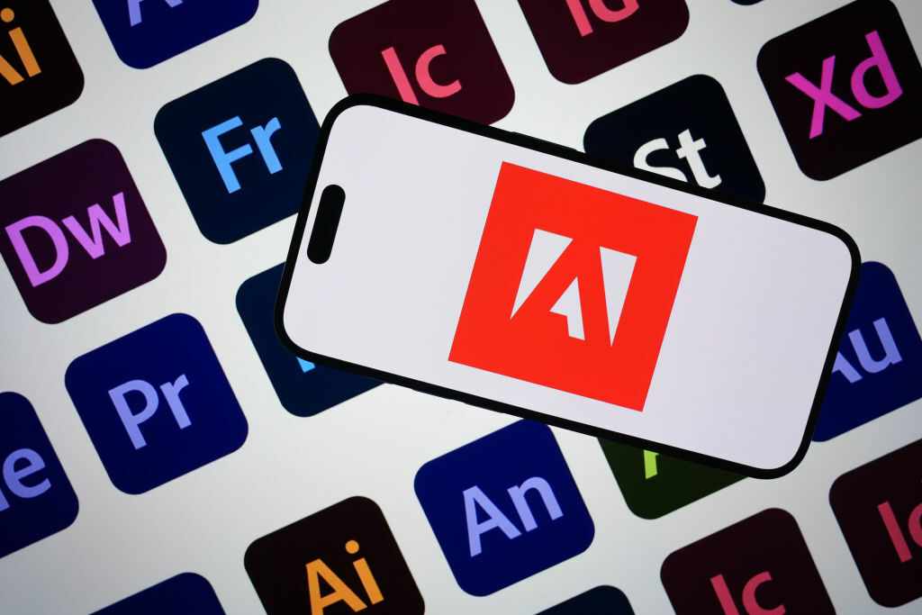 Adobe logo on a smartphone screen against the backdrop of Adobe program logos 