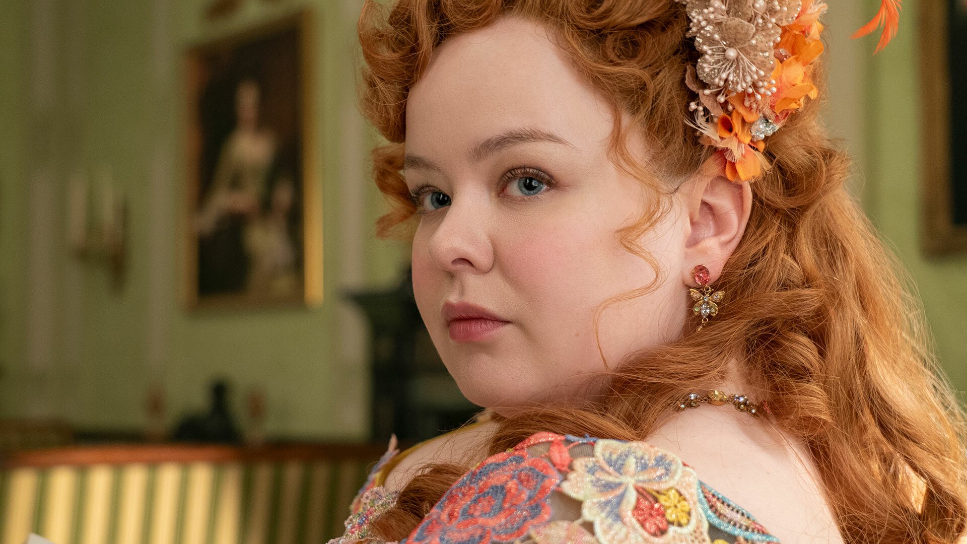 A woman in regency-era dress sits in a lavish room, a book in her hands.