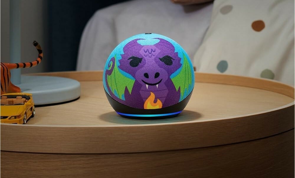 an amazon echo dot kids circular speaker with a colorful face of a dragon sits on a wood nightstand