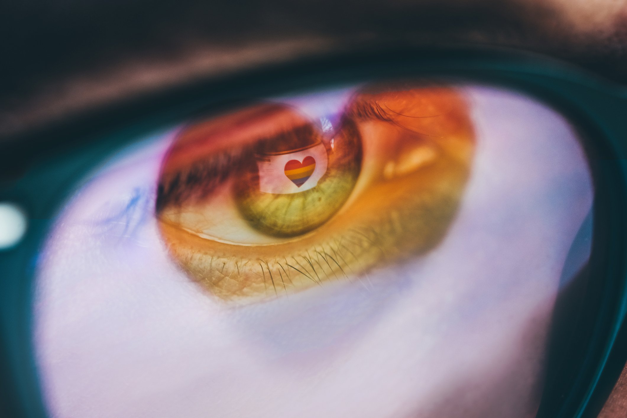 Woman with a rainbow heart reflected in her eyes and glasses.