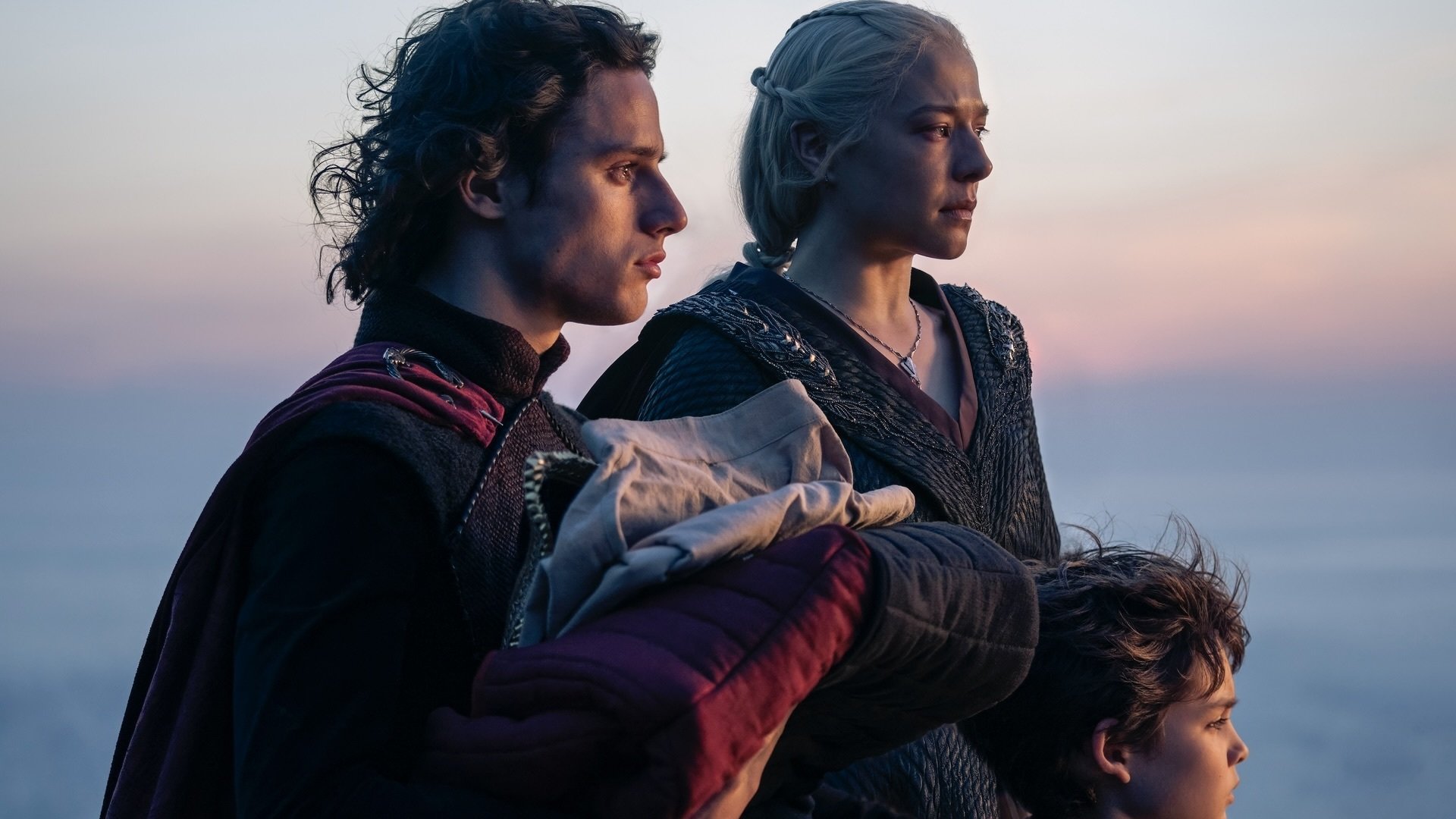 Jacaerys, Rhaenyra, and Joffrey stand together with their backs to the sea and the setting sun.