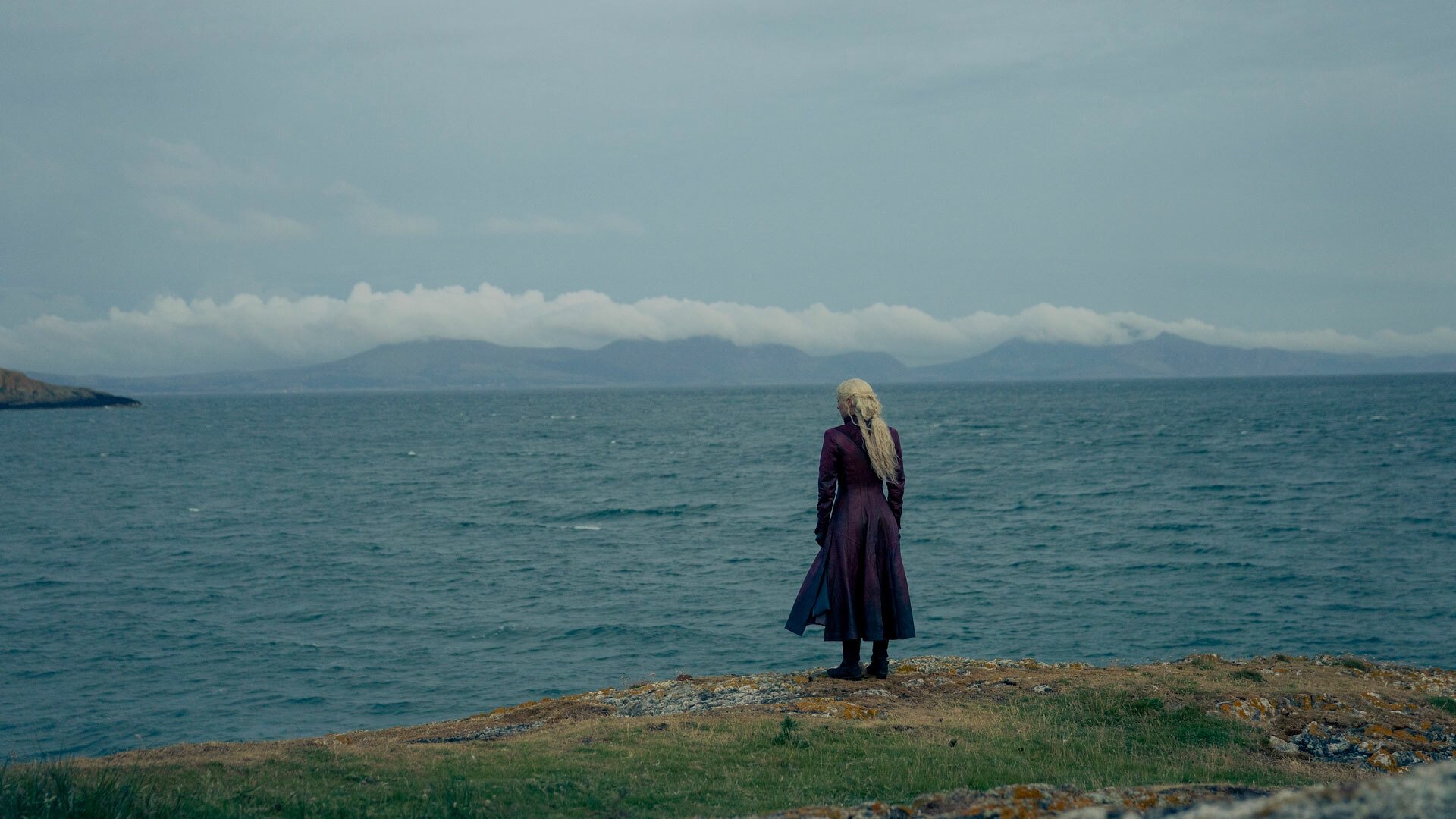 A woman stands on the edge of a large body of water, facing away from the camera.