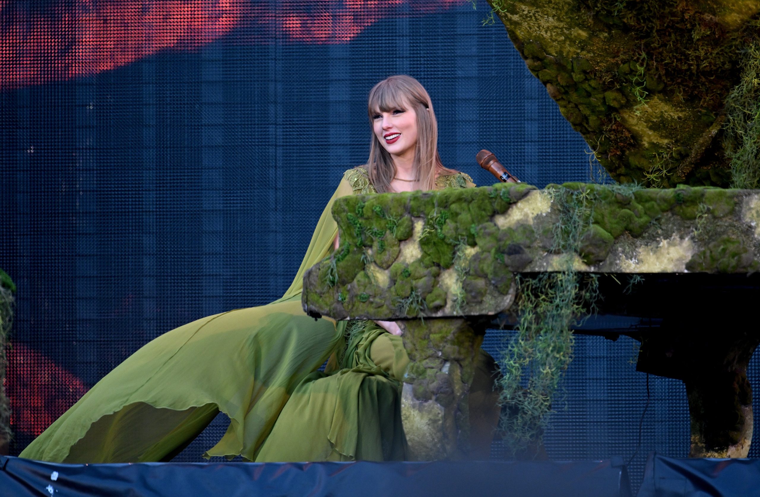 Taylor Swift sitting at a piano in a green dress. 