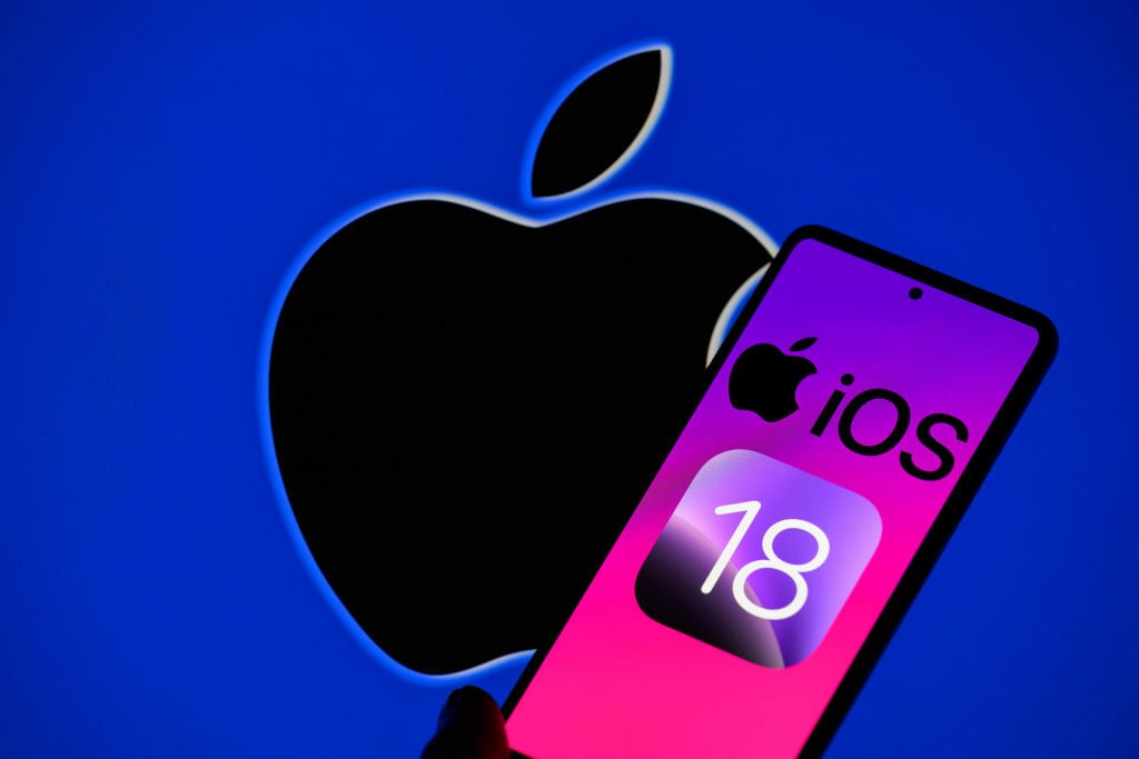 The Apple iOS 18 logo is being displayed on a smartphone with the Apple logo in the background