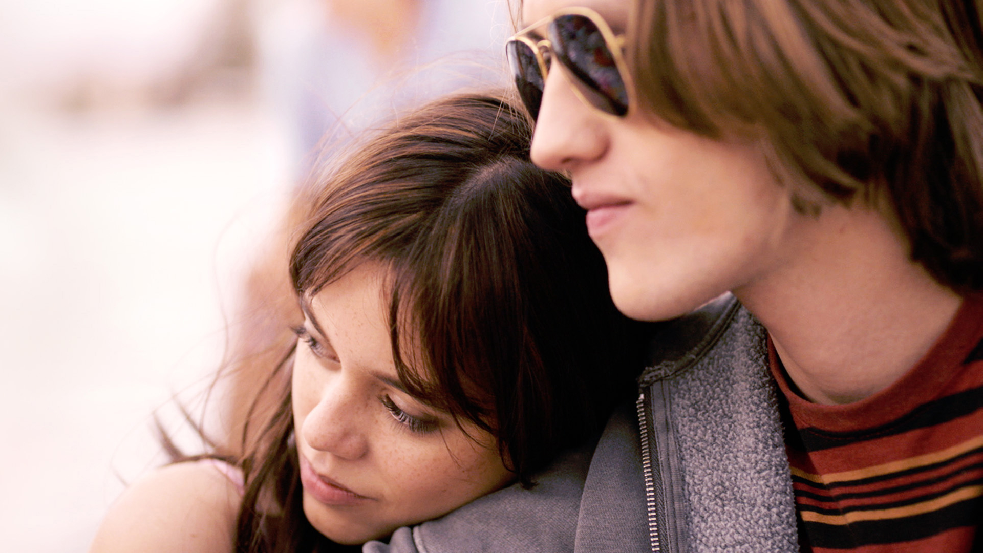 A young woman leans on the shoulder of a young man in sunglasses.