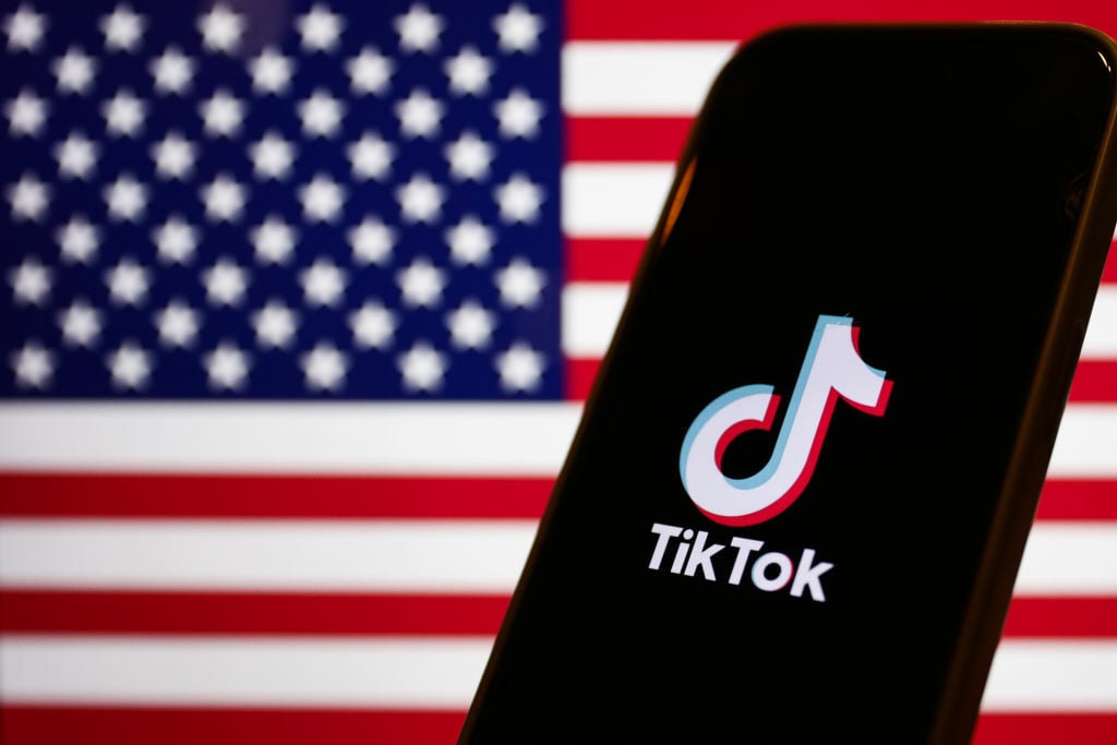 American flag displayed on a laptop screen and TikTok logo displayed on a phone screen.