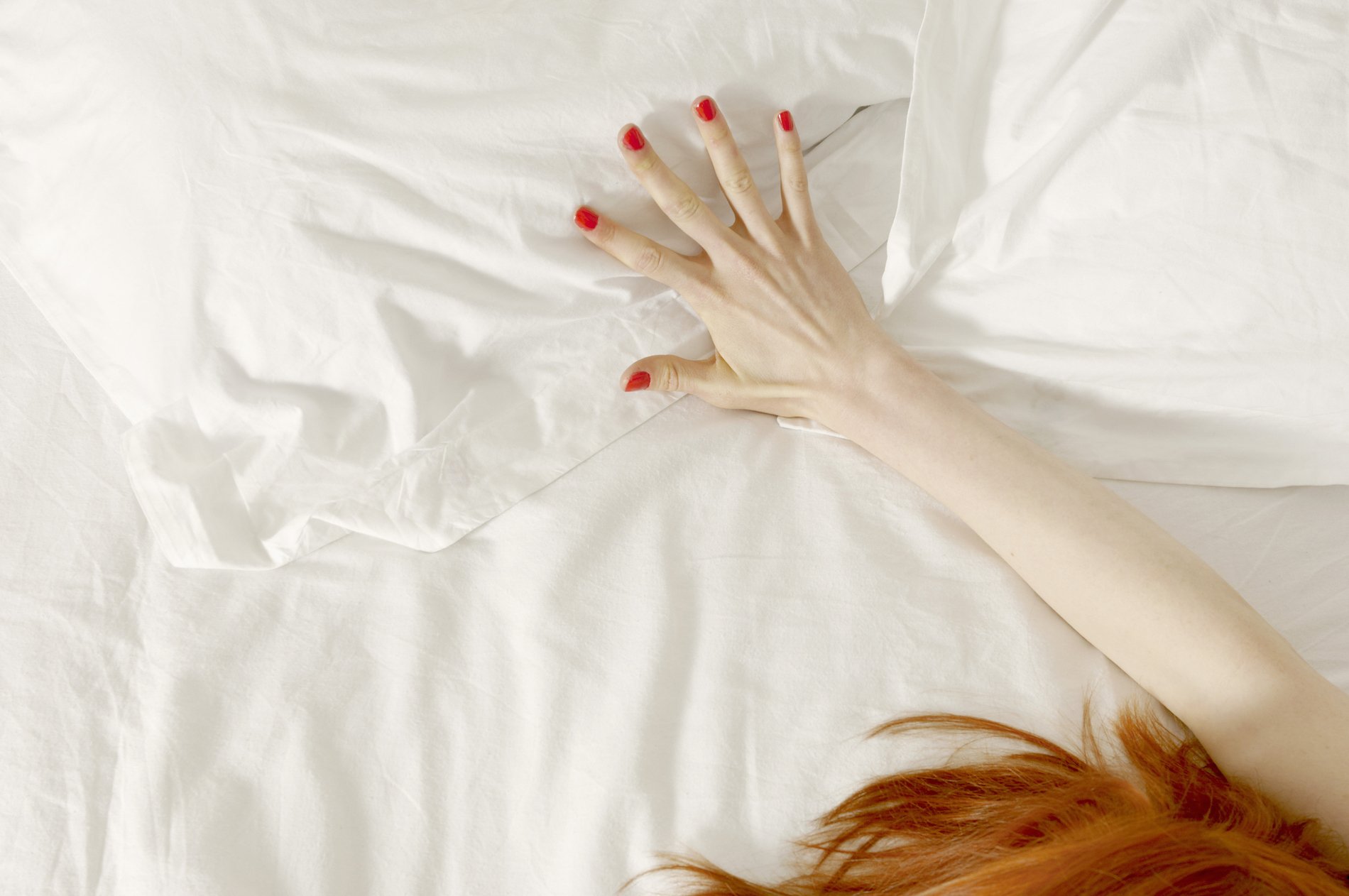 A woman's hand outstretched on white bedsheets, her red hair visible in the bottom corner of the photo. 