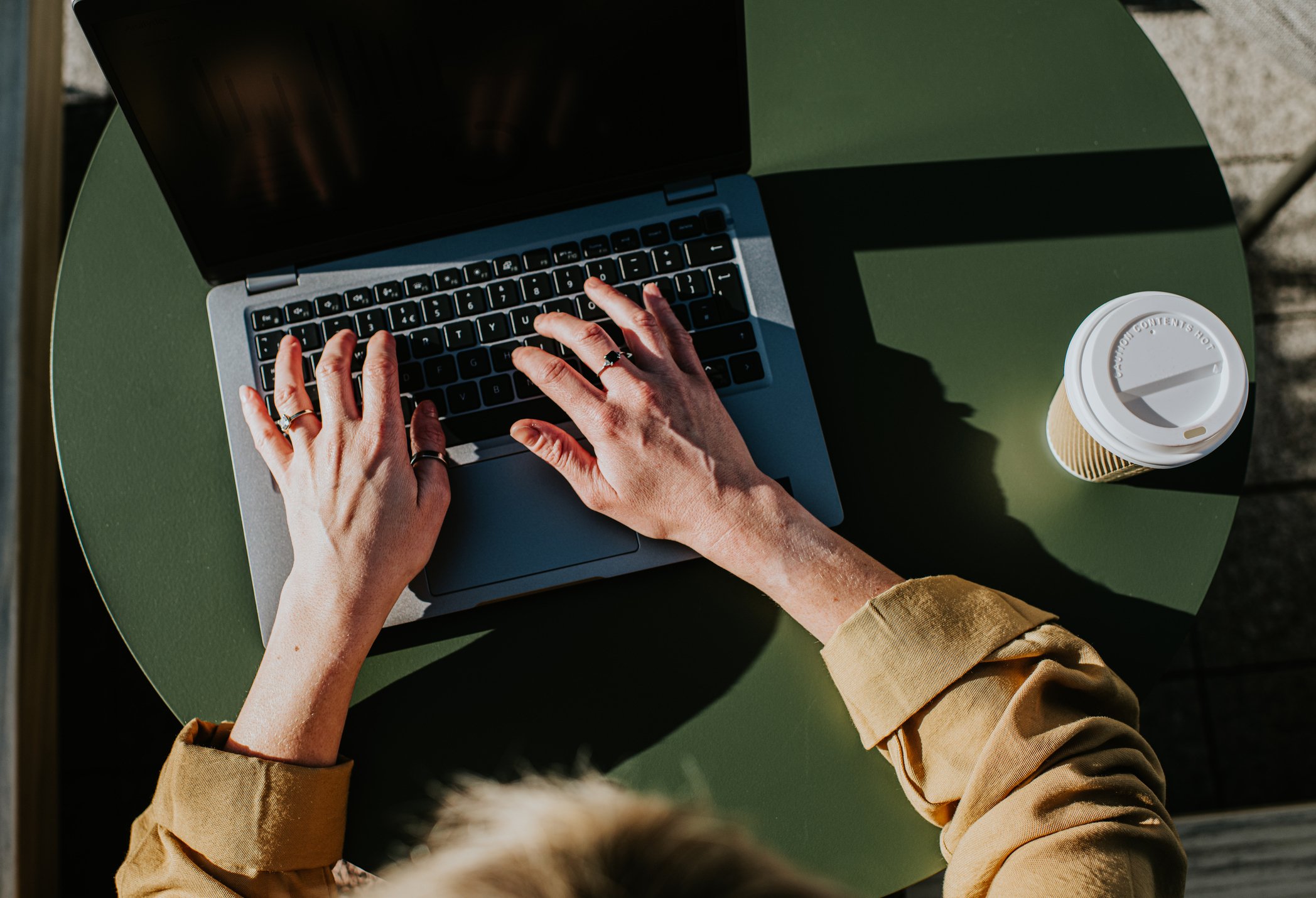 Woman typing on Mac on green table with coffee cup