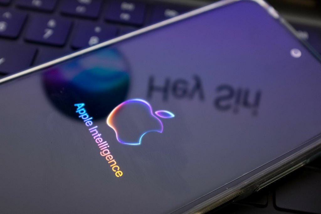  The Apple Intelligence logo is being displayed on a smartphone, with the Apple Siri logo in the background,