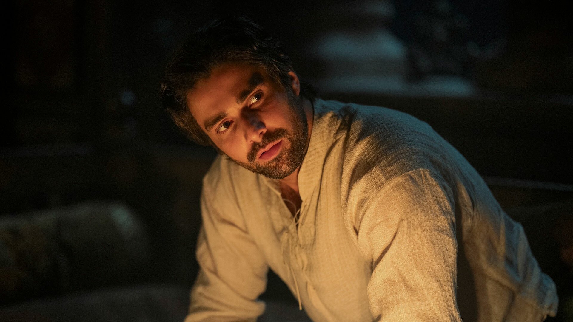 A man sits in a dark room, looking serious.