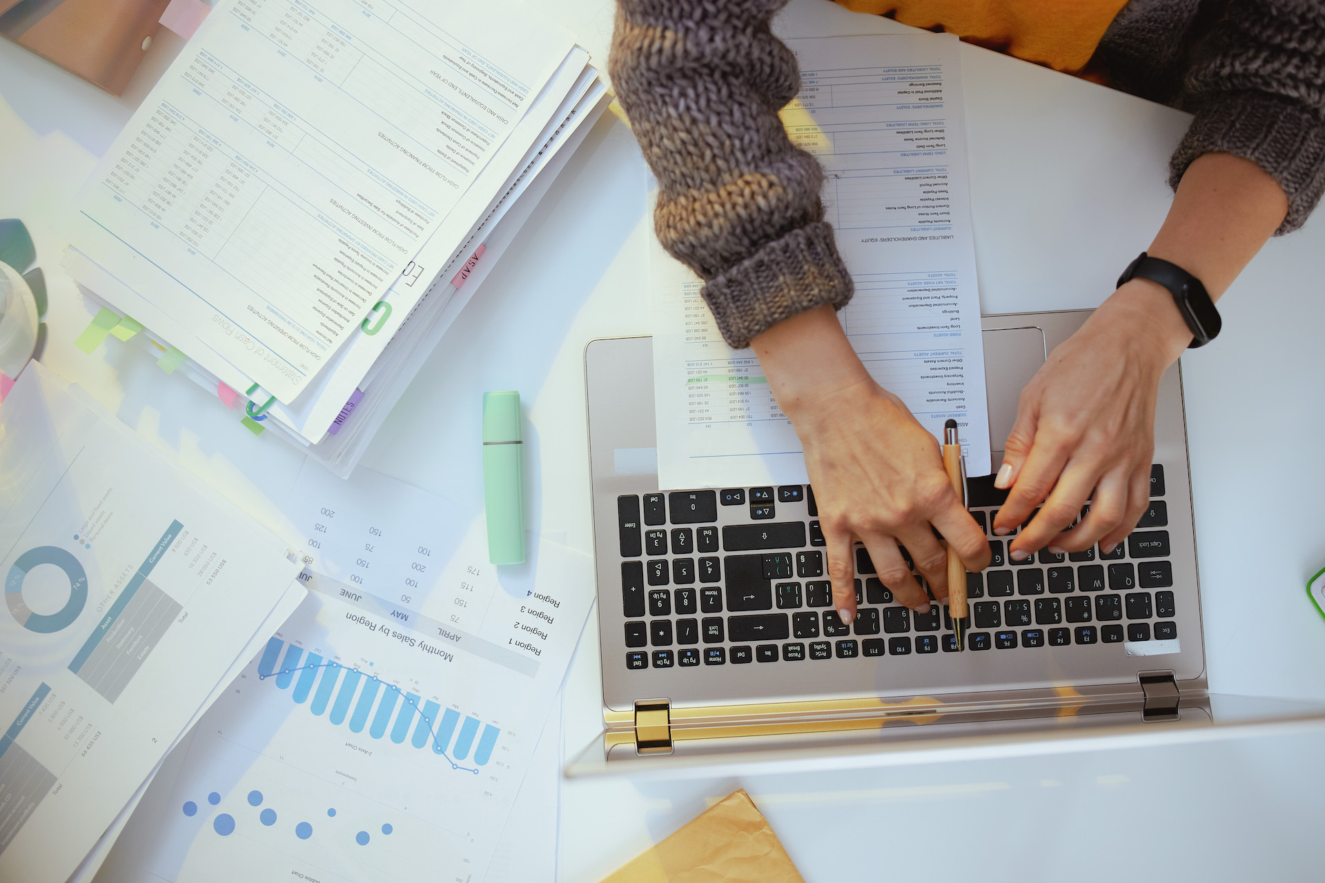 A person has financial paperwork out while working on a computer.